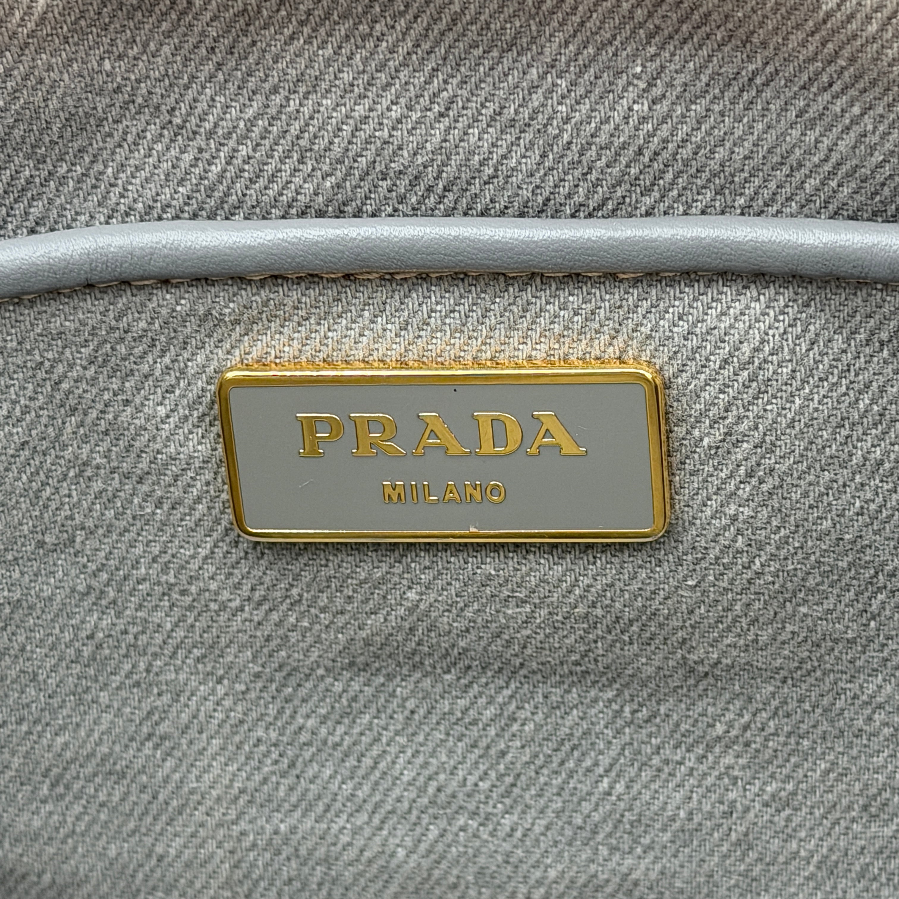 Prada Canapa Tote Bag in grey canvas with rope logo motif and dual top handles against a plain background.