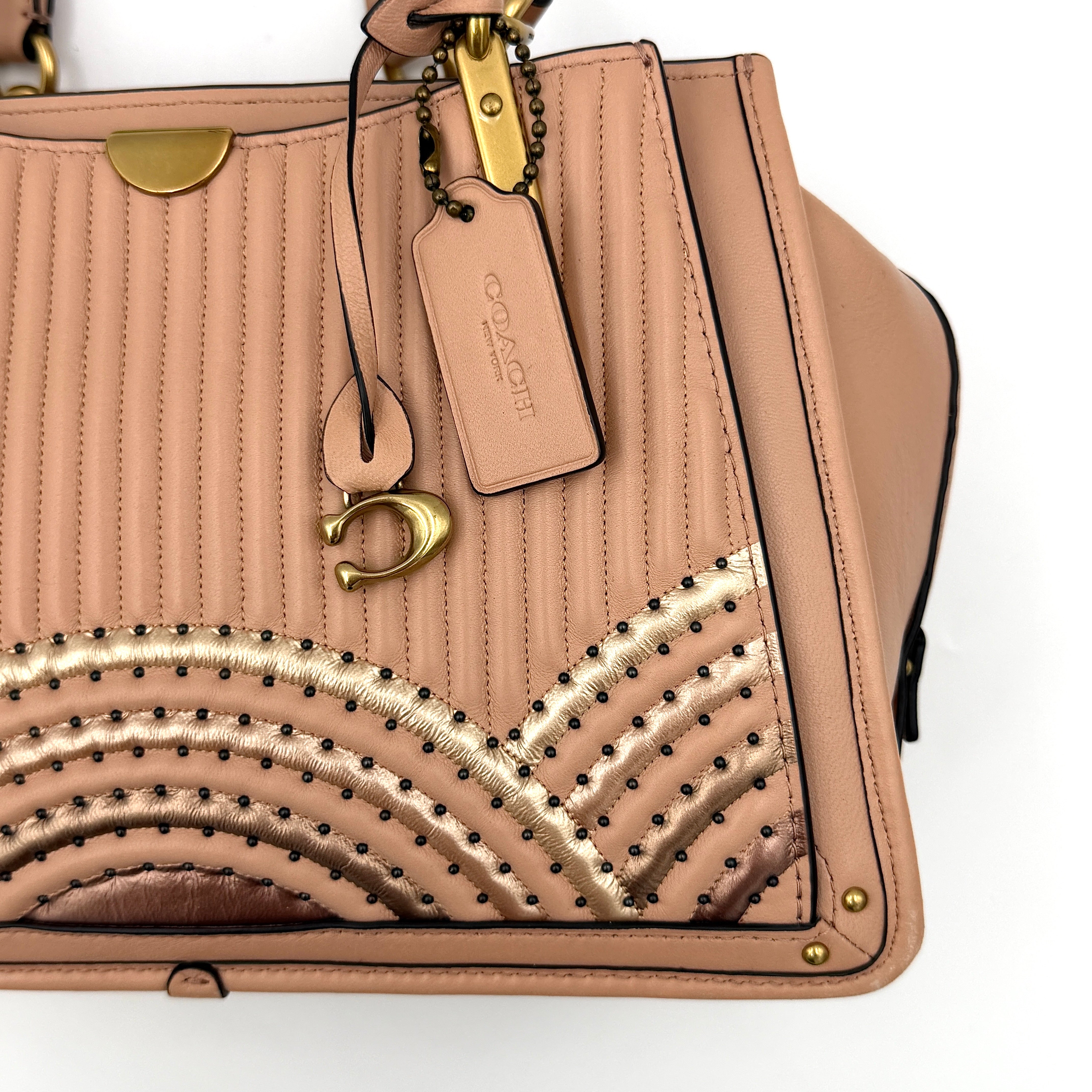 Coach Dreamer 27 handbag in nude pink leather with Deco quilting, gold rivets, and detachable strap, displayed elegantly on a plain background.