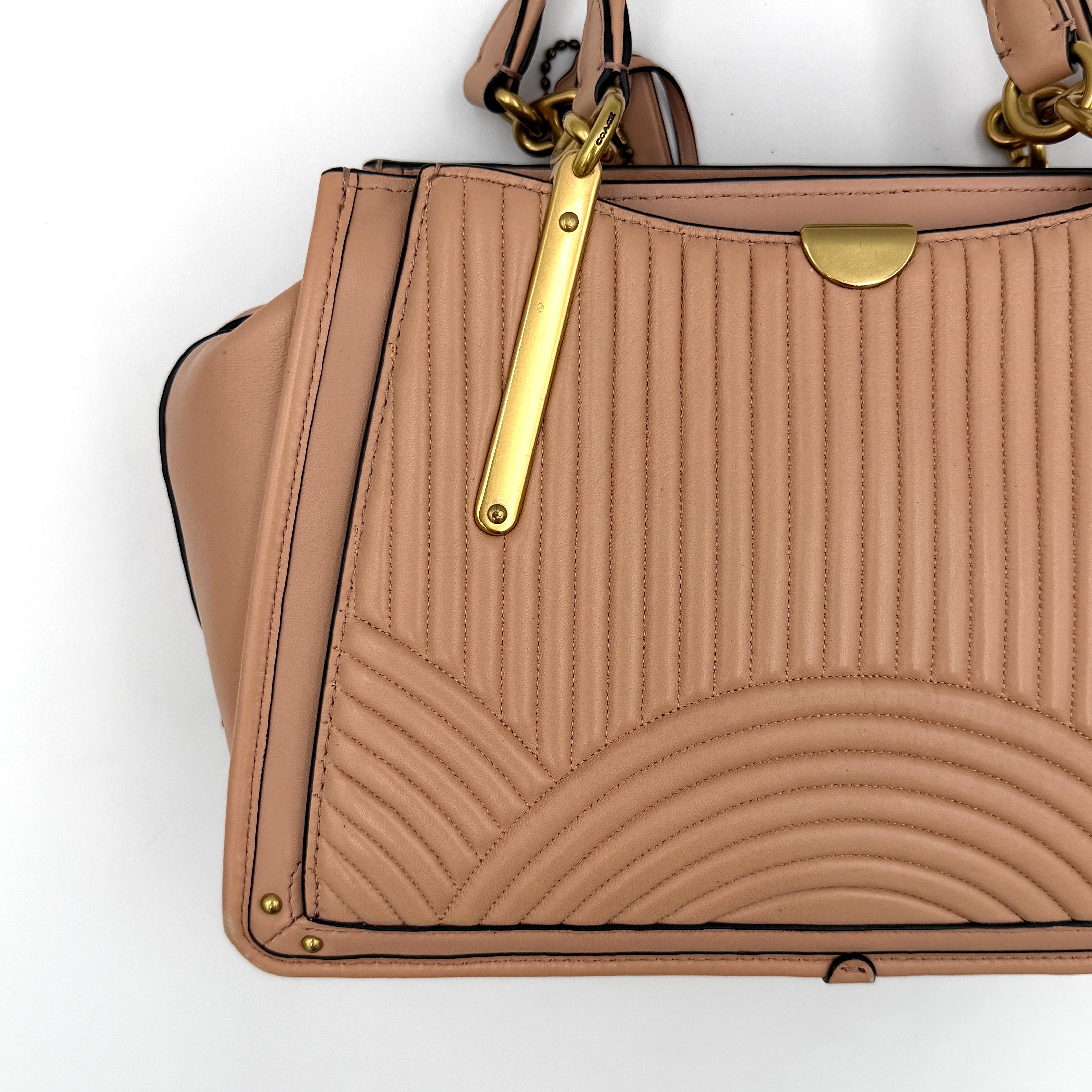 Coach Dreamer 27 handbag in nude pink leather with Deco quilting, gold rivets, and detachable strap, displayed elegantly on a plain background.