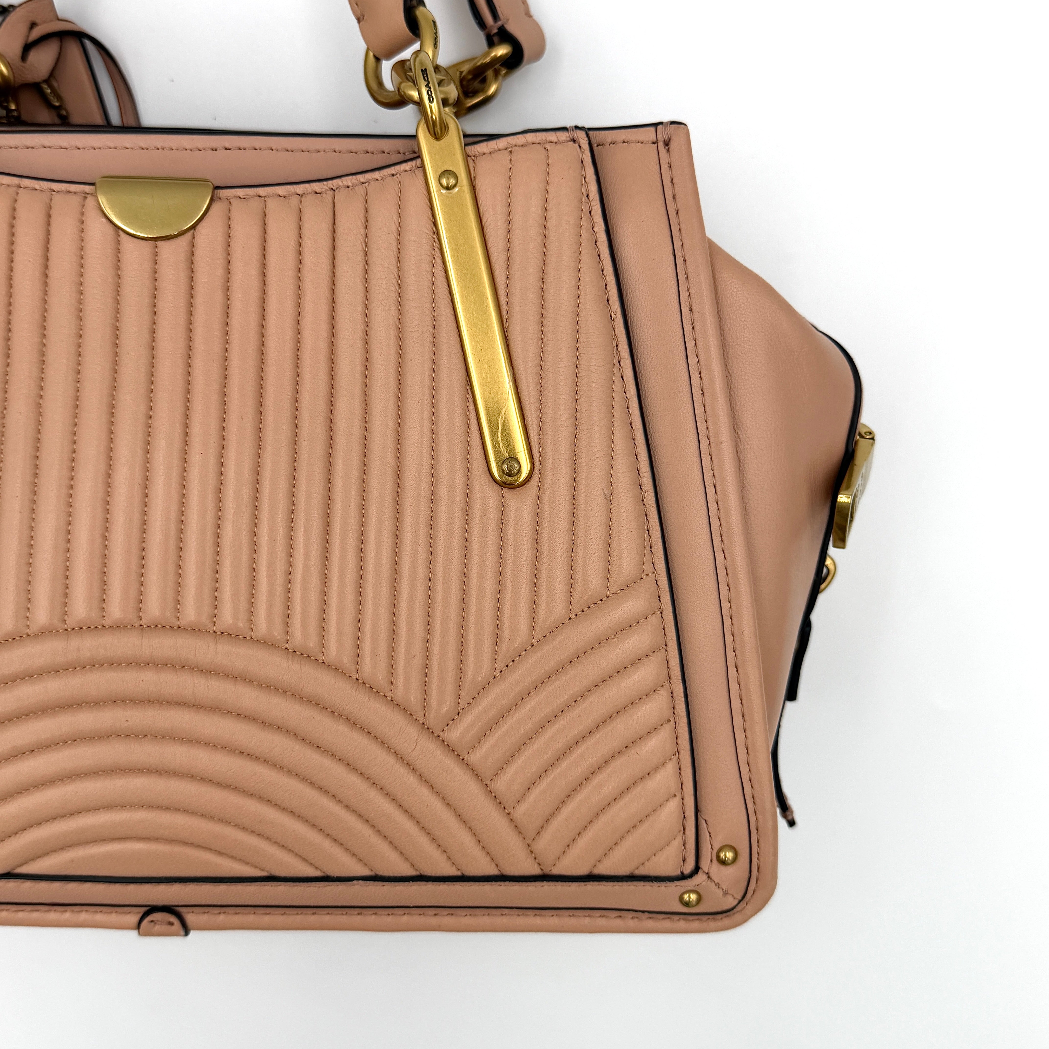 Coach Dreamer 27 handbag in nude pink leather with Deco quilting, gold rivets, and detachable strap, displayed elegantly on a plain background.