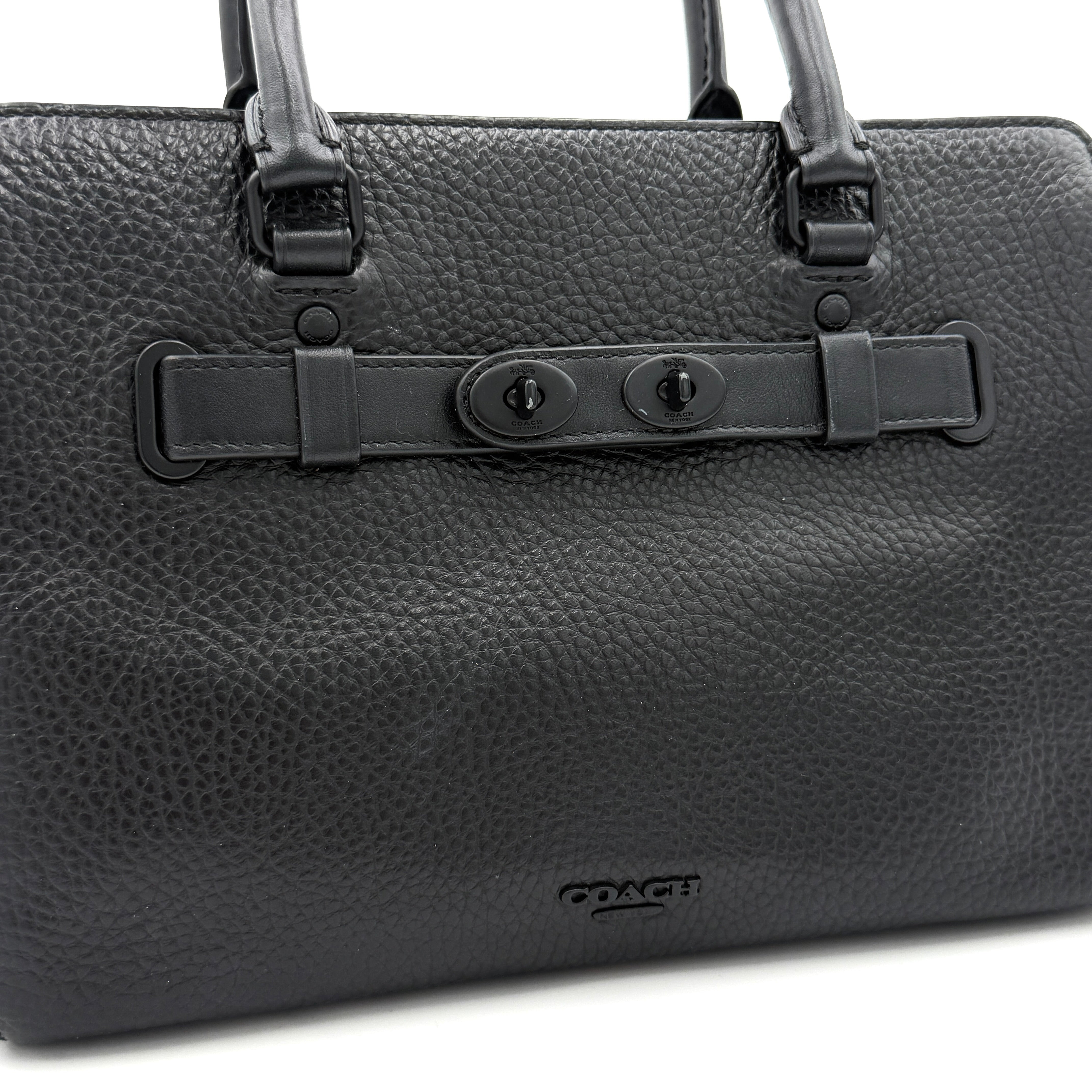 Coach Blake Carryall 25 bag in black pebbled leather with dual top handles, detachable strap, and front turnlock accents.