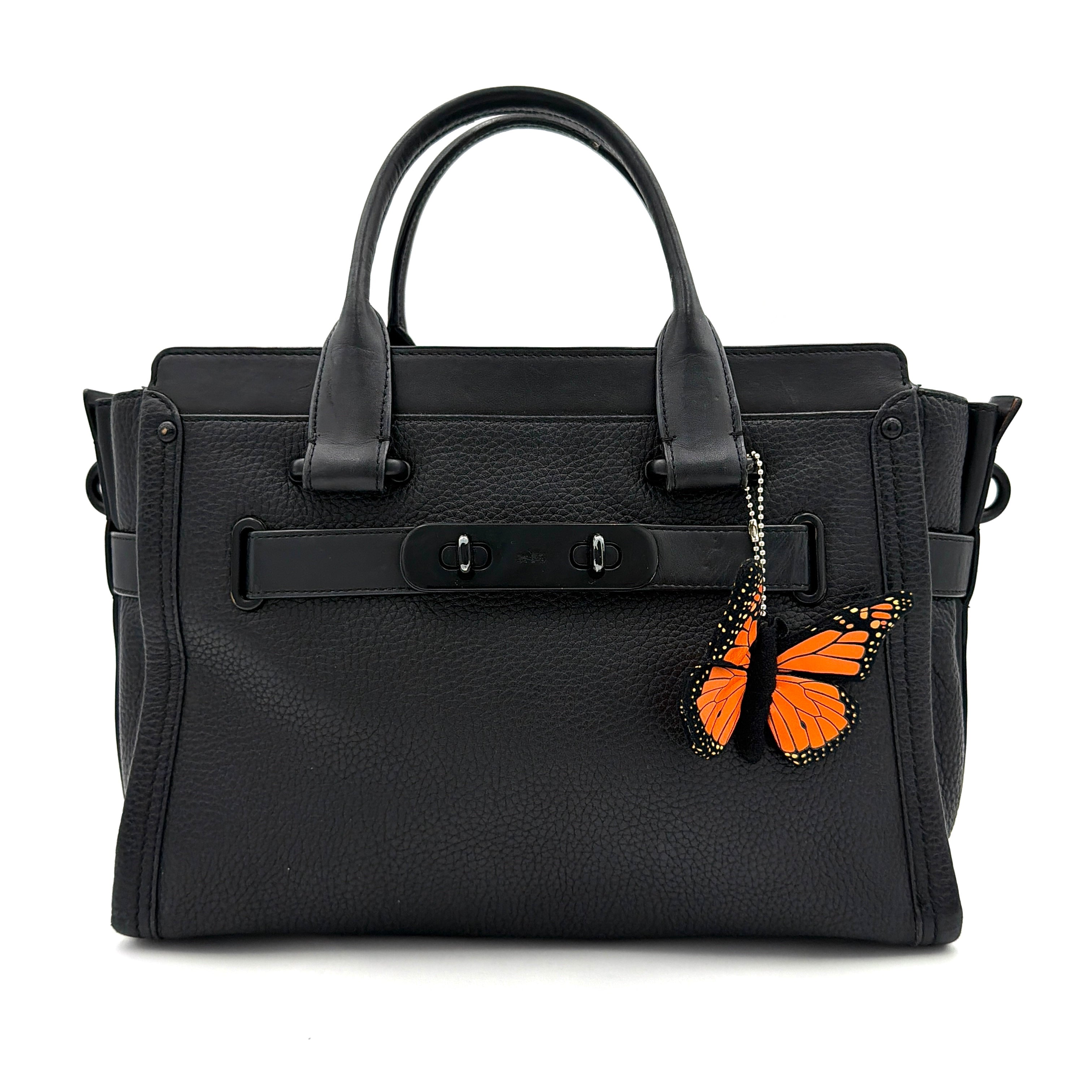 Coach Swagger Carryall handbag in black pebbled leather with matte black hardware and a vibrant orange butterfly charm.