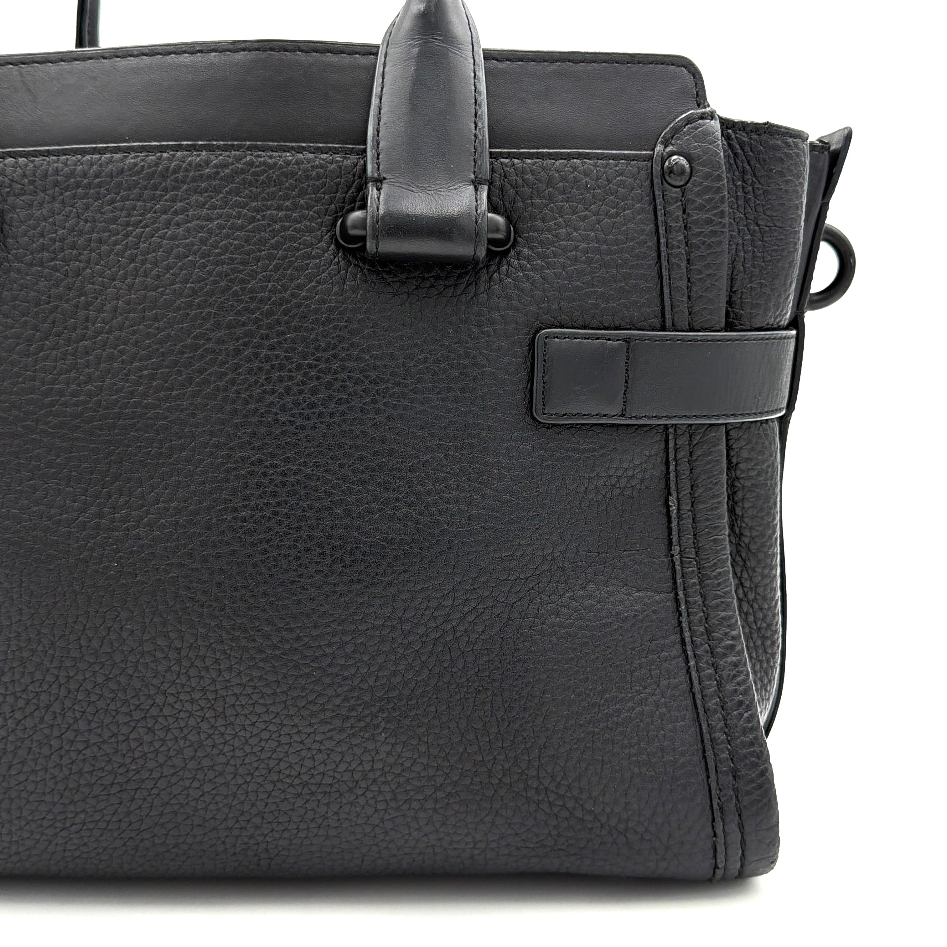 Coach Swagger Carryall handbag in black pebbled leather with matte black hardware and a vibrant orange butterfly charm.