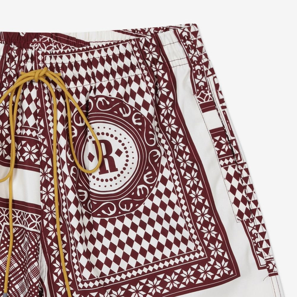 Rhude maroon and white swim shorts with a card print pattern and yellow drawstring, presented flat.
