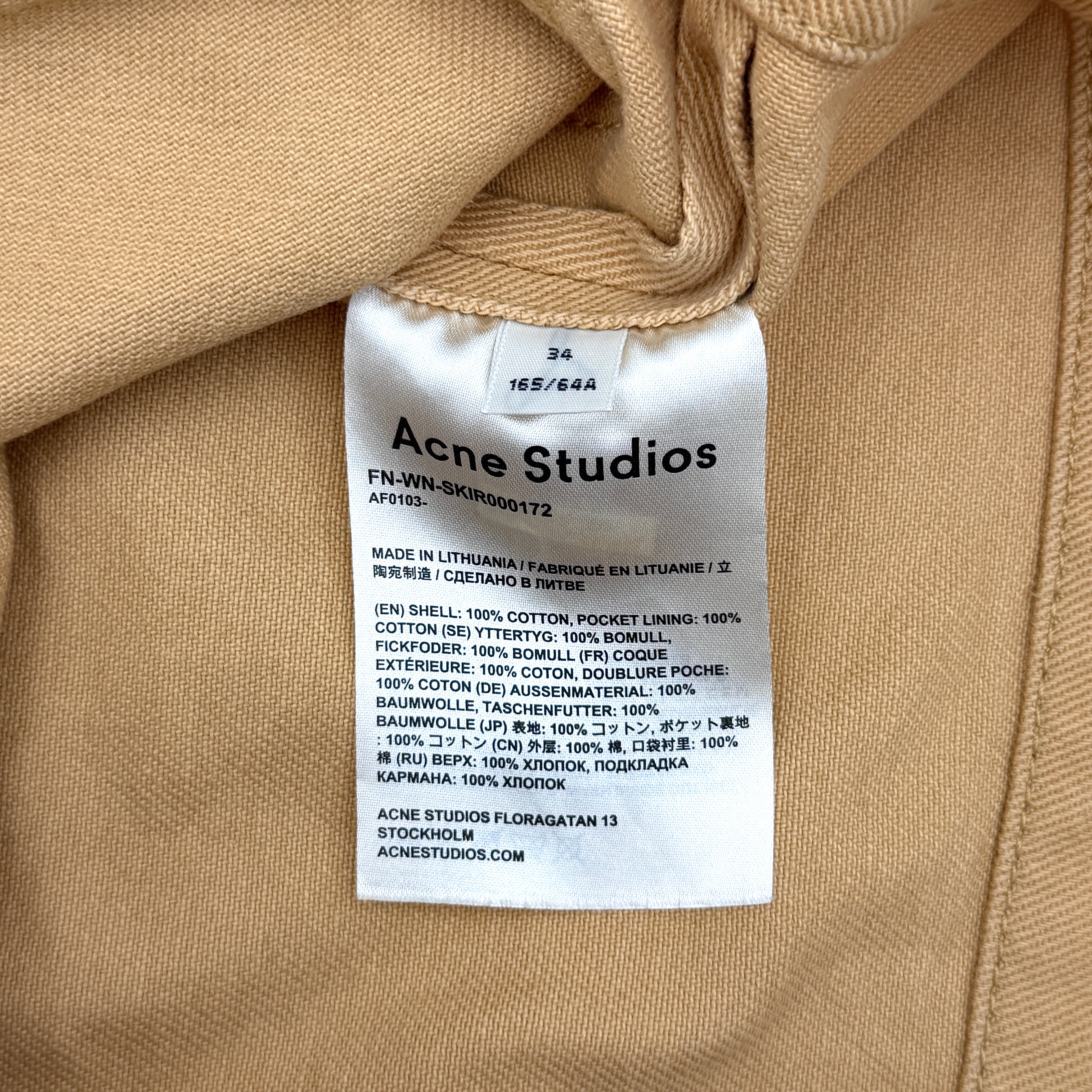 Acne Studios cream and tan cotton drill mini skirt with oversized flap pockets and front button closure, styled flat.