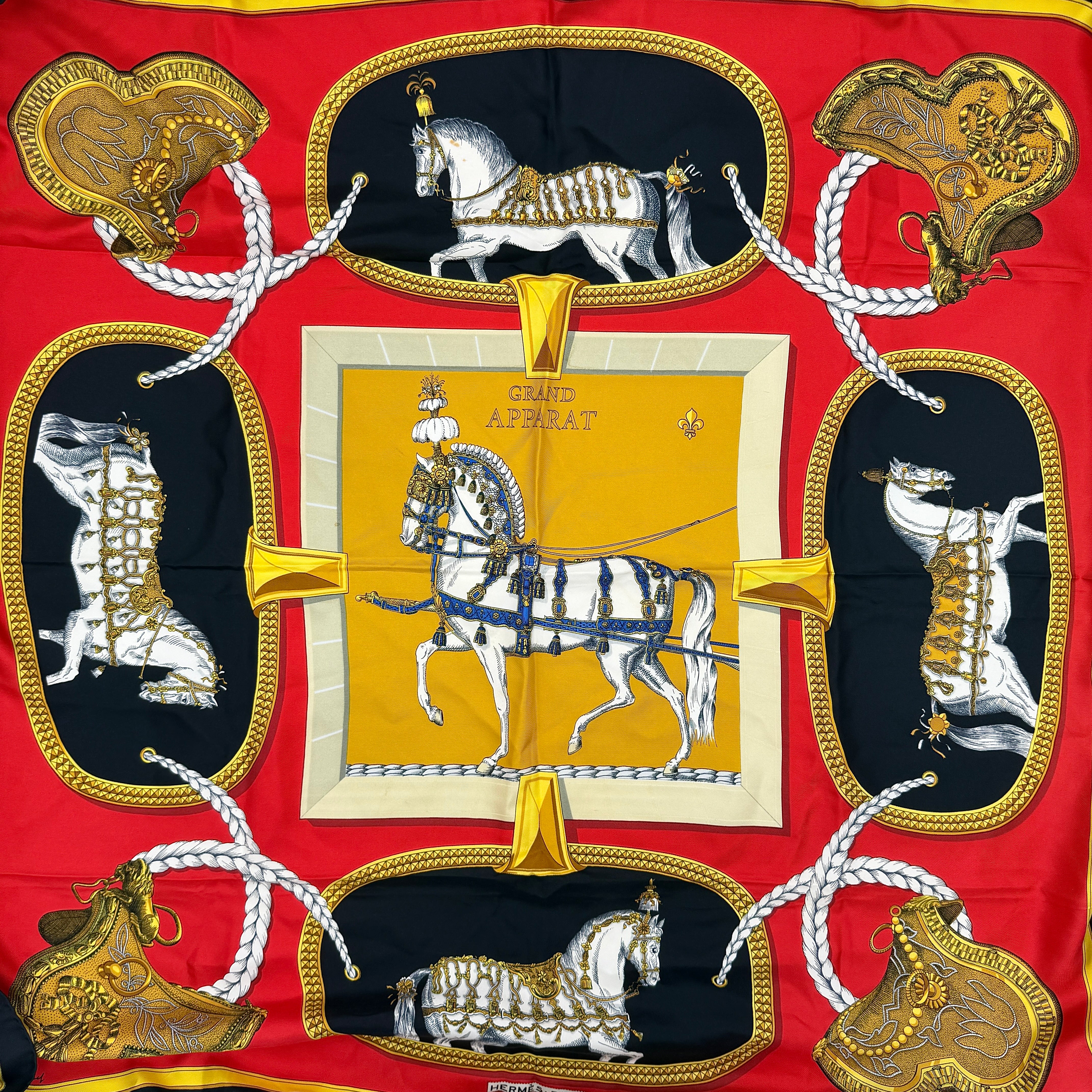 Hermès Grand Apparat silk scarf, featuring an ornate equestrian motif in rich red, gold, and black, elegantly folded to showcase its intricate print.