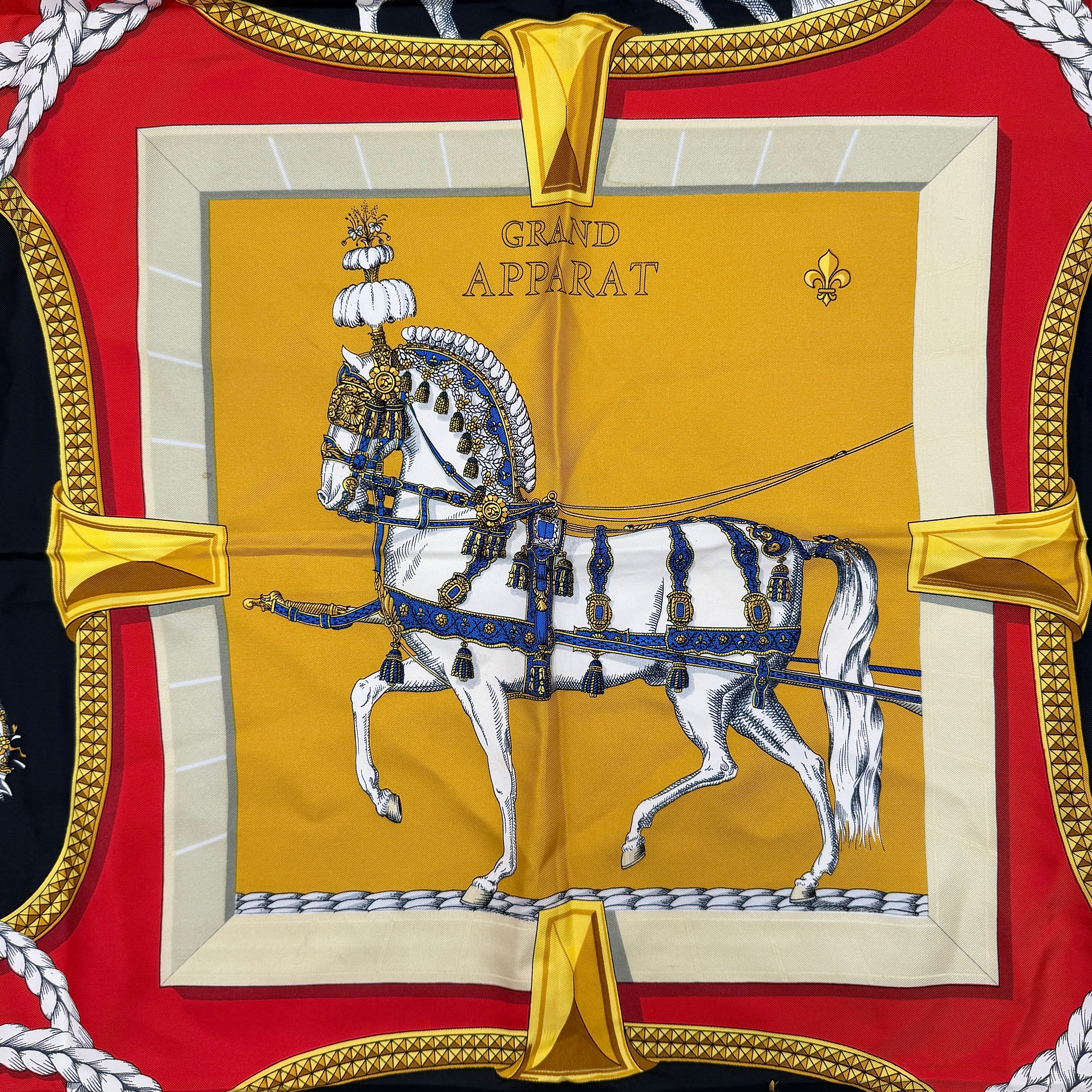 Hermès Grand Apparat silk scarf, featuring an ornate equestrian motif in rich red, gold, and black, elegantly folded to showcase its intricate print.