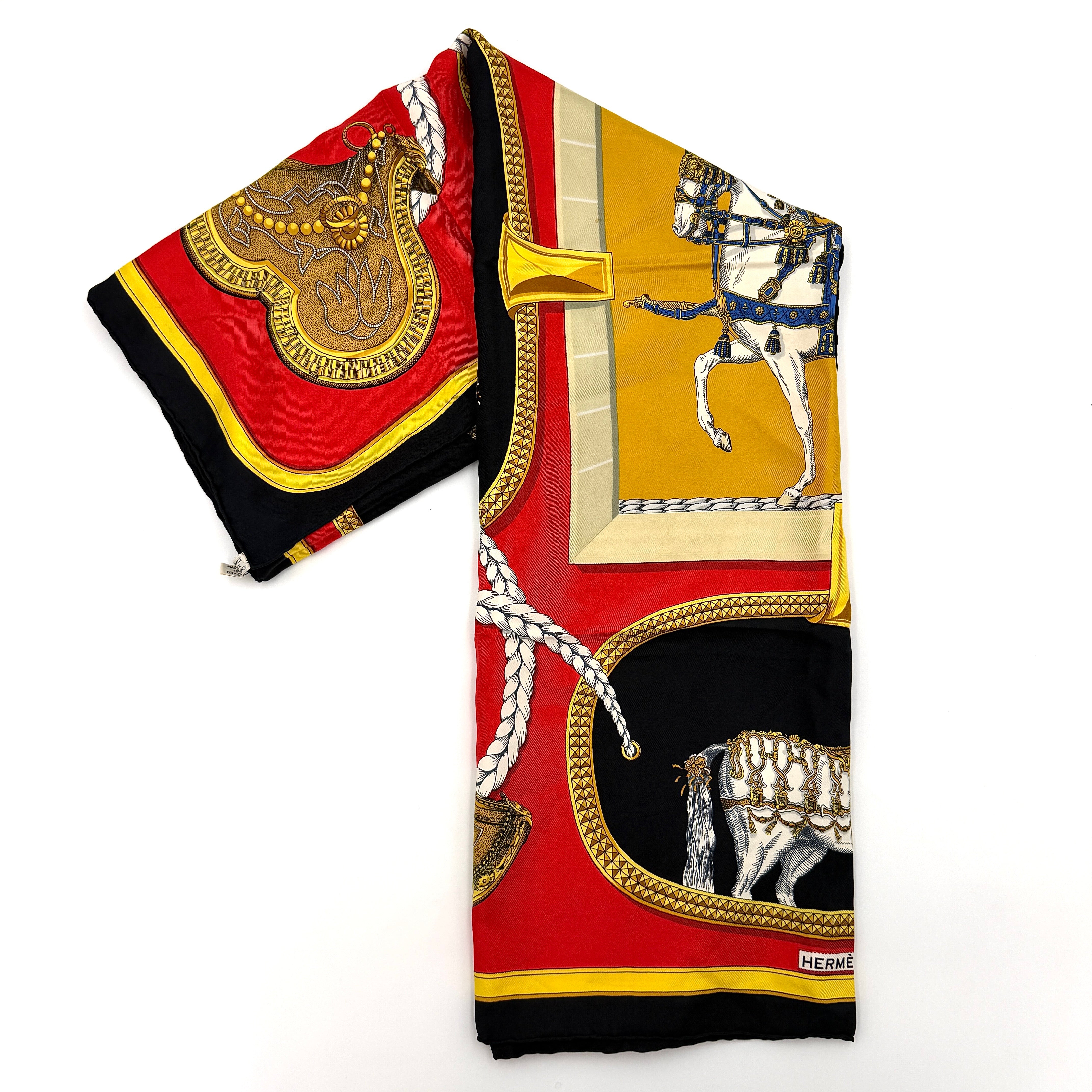 Hermès Grand Apparat silk scarf, featuring an ornate equestrian motif in rich red, gold, and black, elegantly folded to showcase its intricate print.