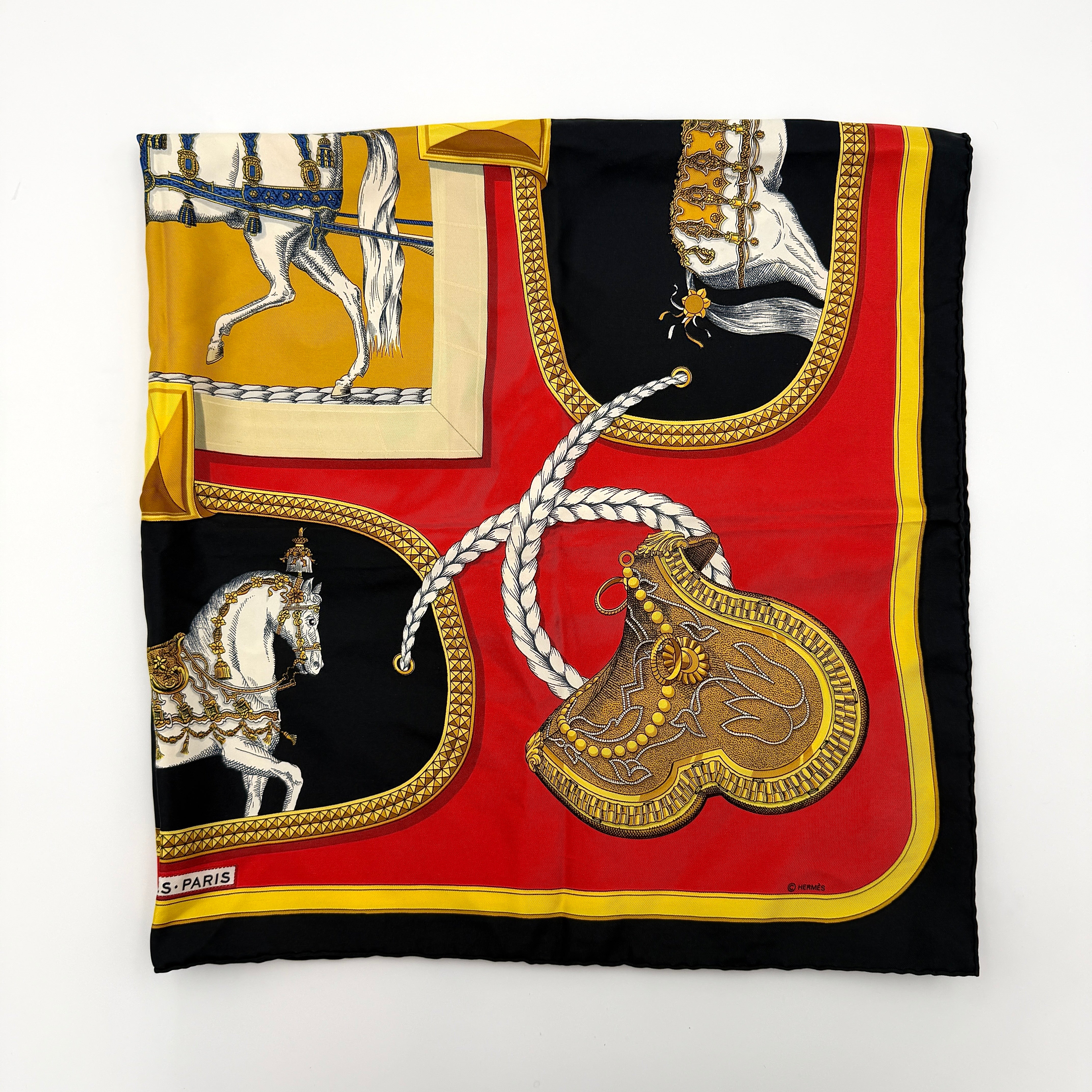 Hermès Grand Apparat silk scarf, featuring an ornate equestrian motif in rich red, gold, and black, elegantly folded to showcase its intricate print.