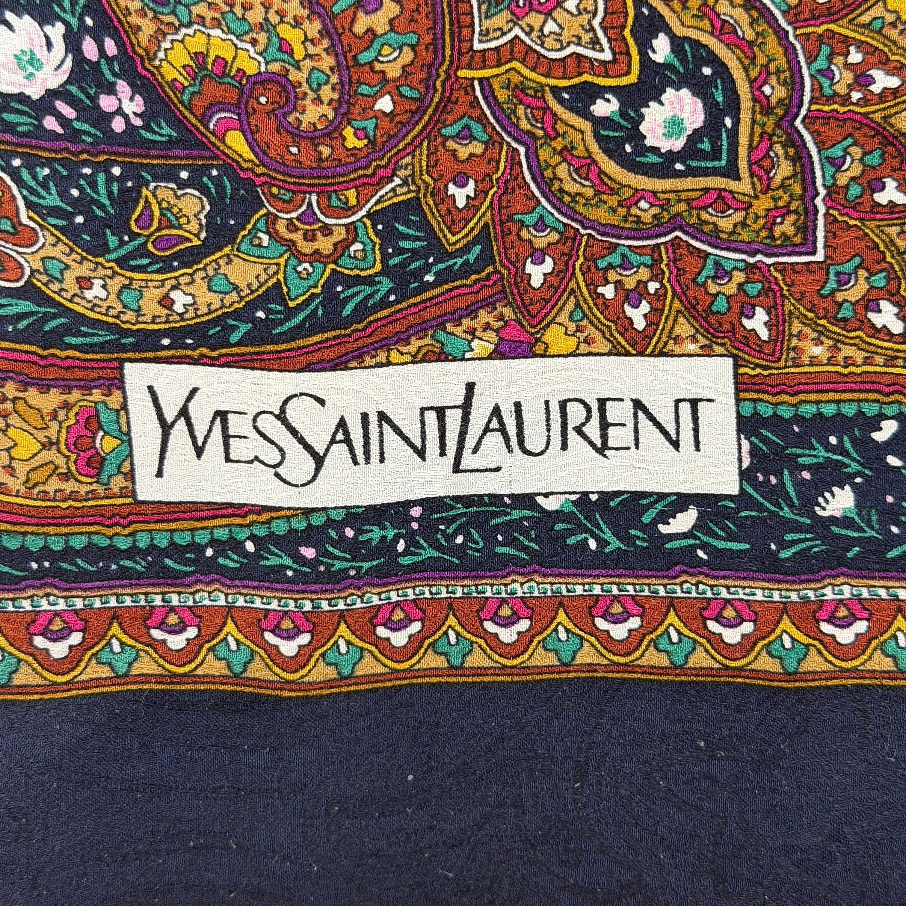 A Saint Laurent cotton scarf in multicolour paisley, elegantly folded to reveal its intricate pattern and ochre border.
