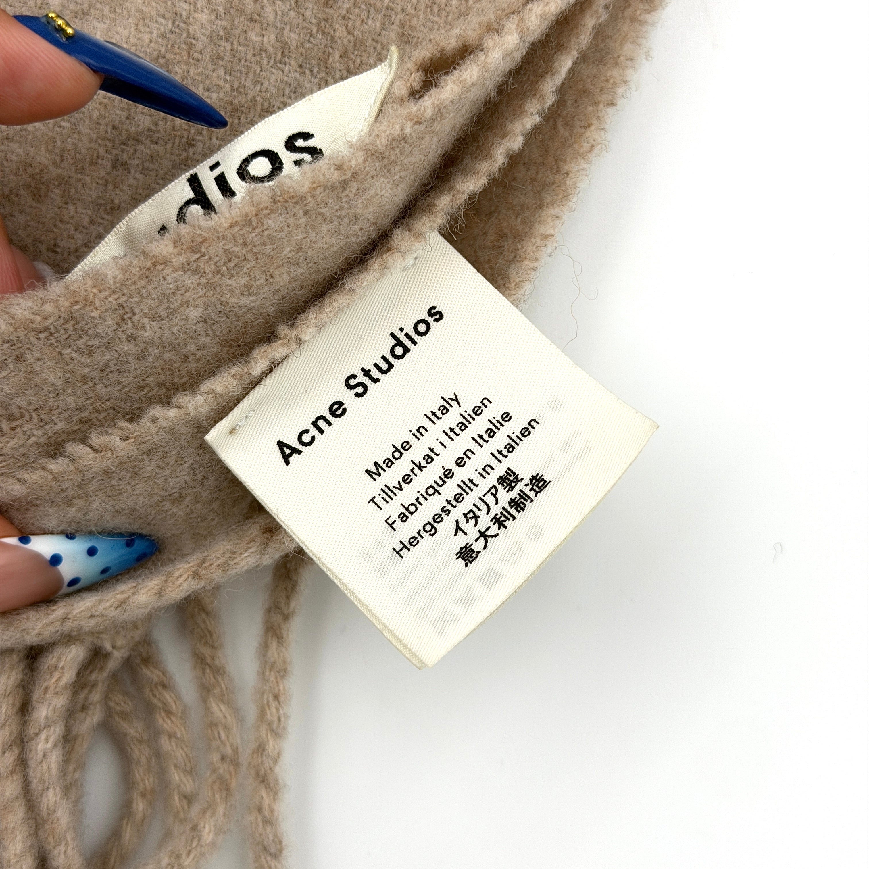Acne Studios wool scarf in soft light brown with a fringed edge and signature label at the hem.