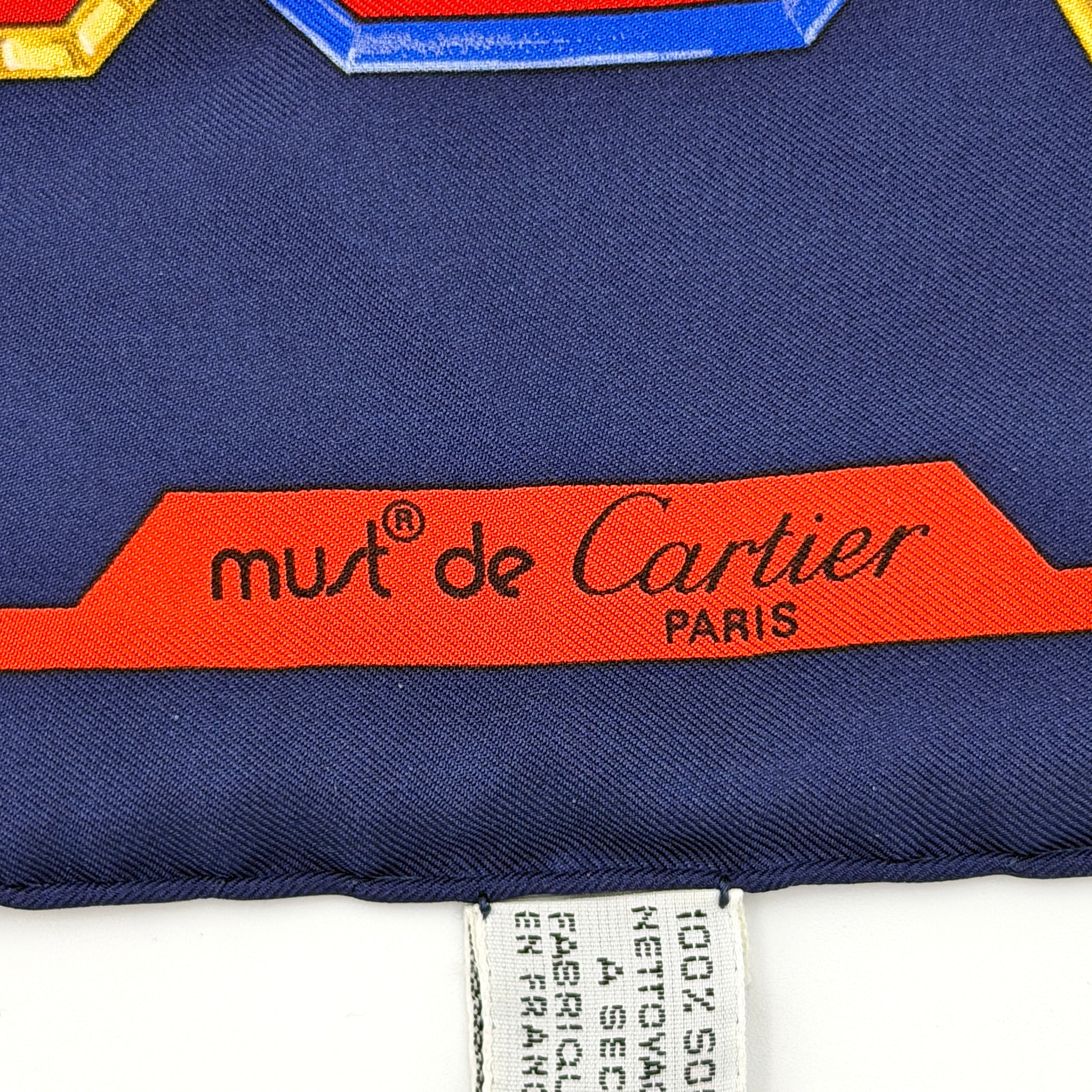 Cartier Must de Cartier silk scarf with striking navy, red, and gold chain motif and jewel accents, styled in a folded drape.