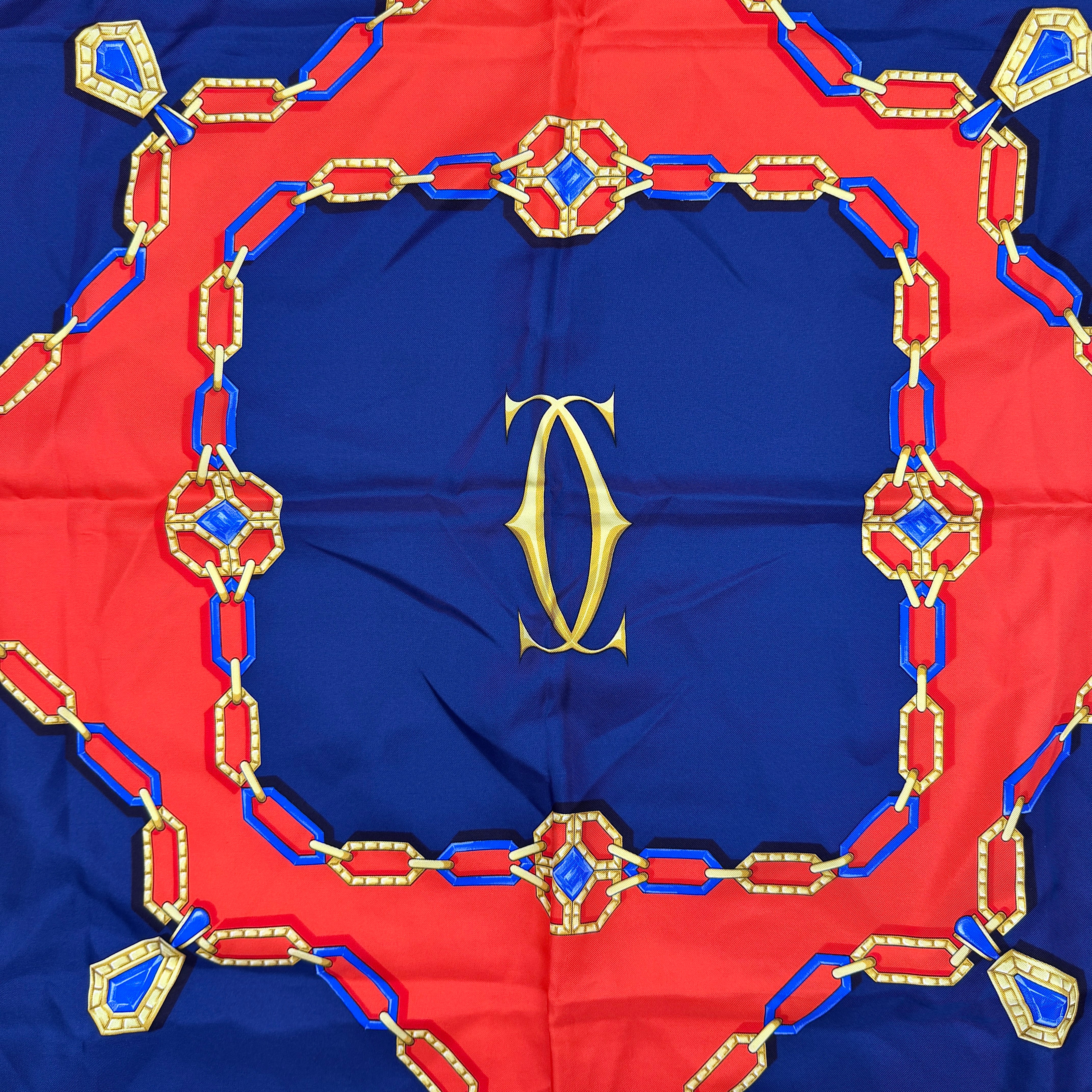 Cartier Must de Cartier silk scarf with striking navy, red, and gold chain motif and jewel accents, styled in a folded drape.