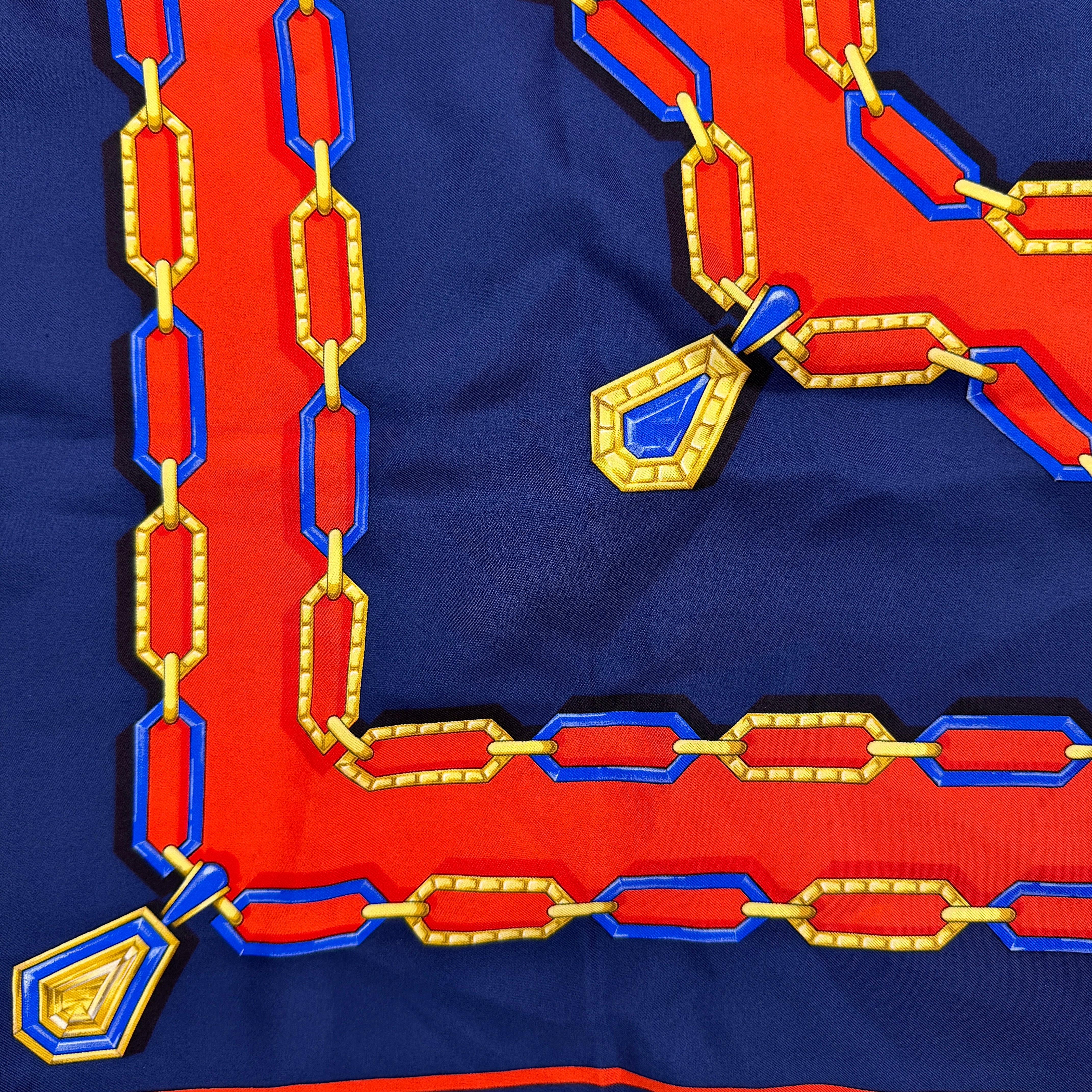 Cartier Must de Cartier silk scarf with striking navy, red, and gold chain motif and jewel accents, styled in a folded drape.