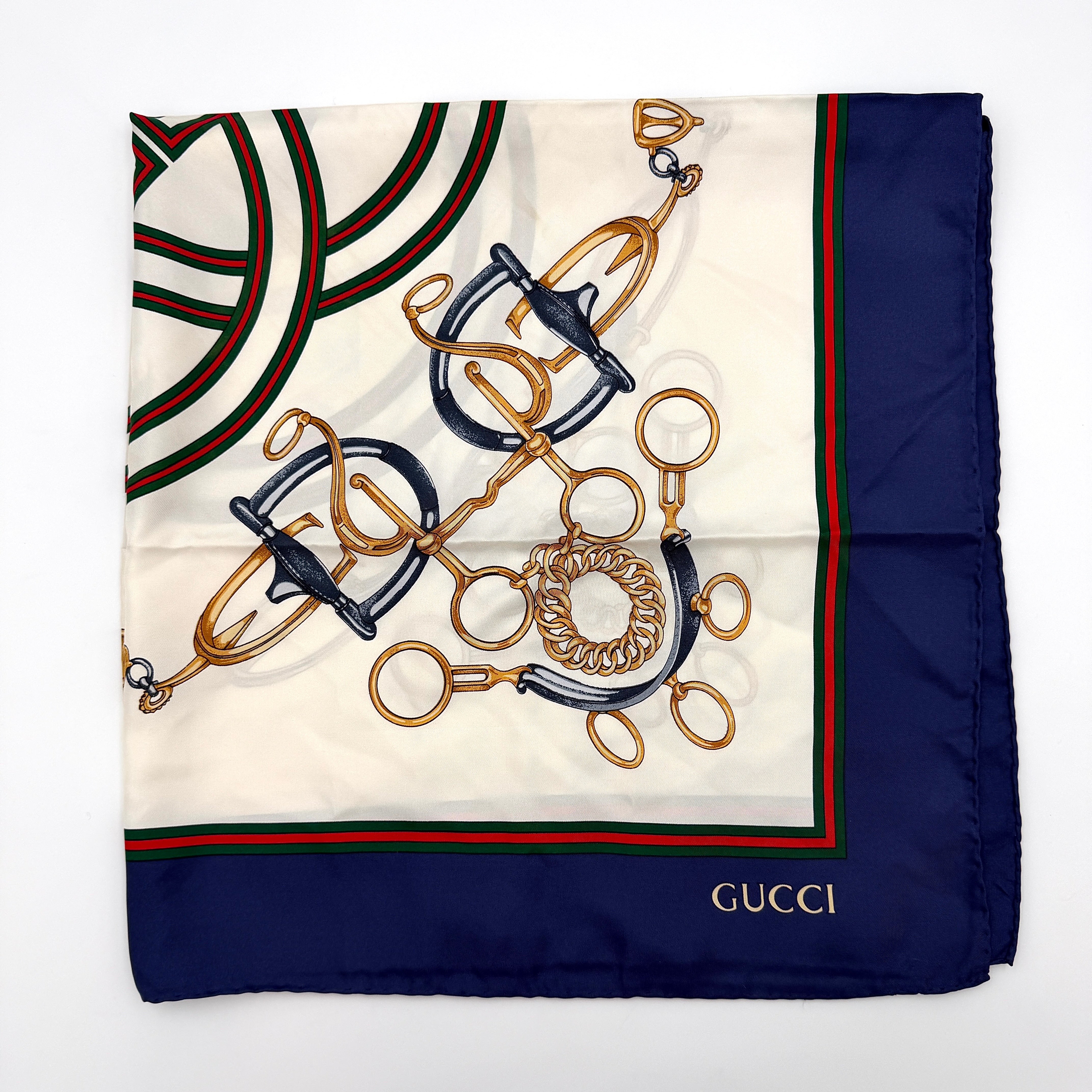 Gucci silk scarf with equestrian horsebit print, navy borders, and large GG logo displayed against a white background.