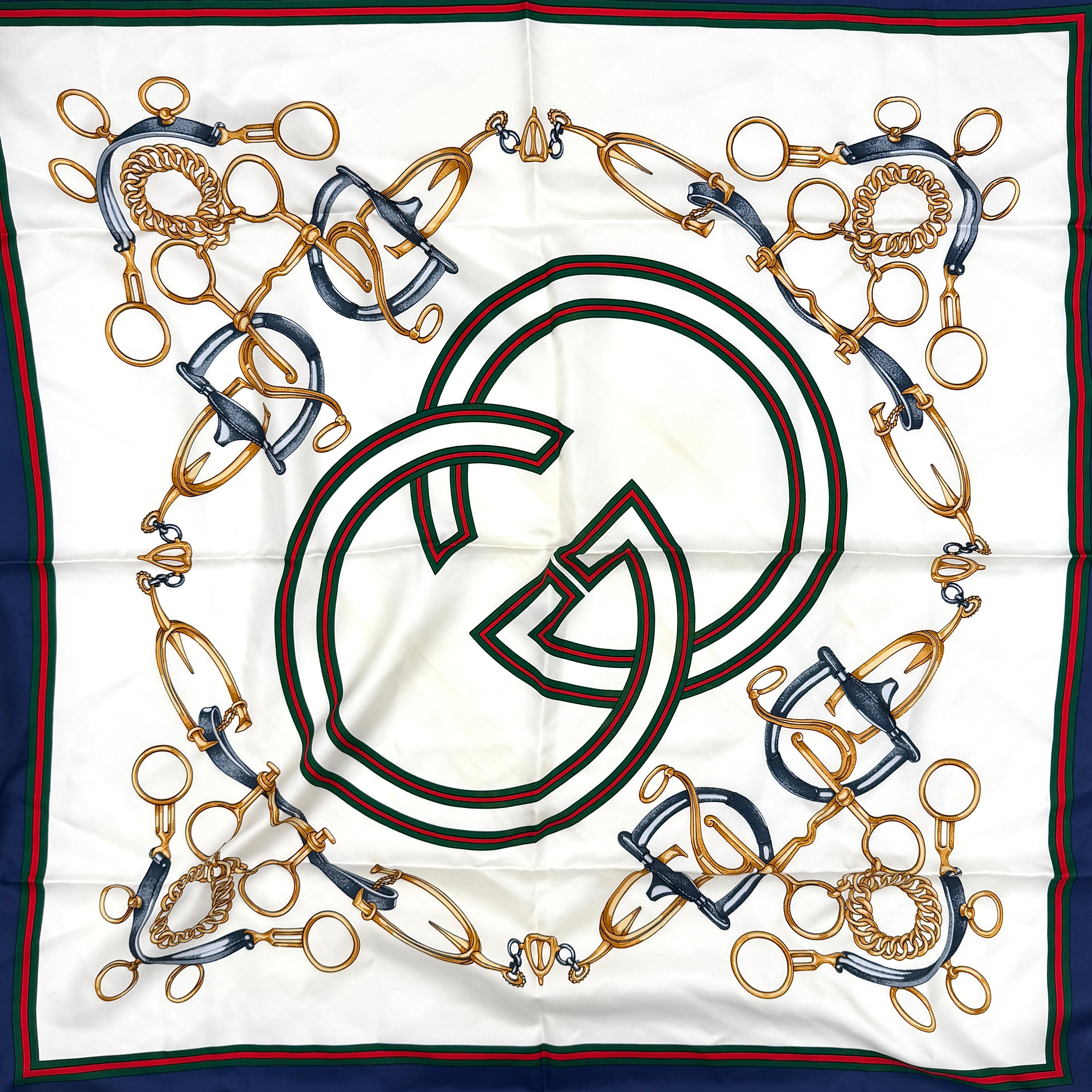 Gucci silk scarf with equestrian horsebit print, navy borders, and large GG logo displayed against a white background.
