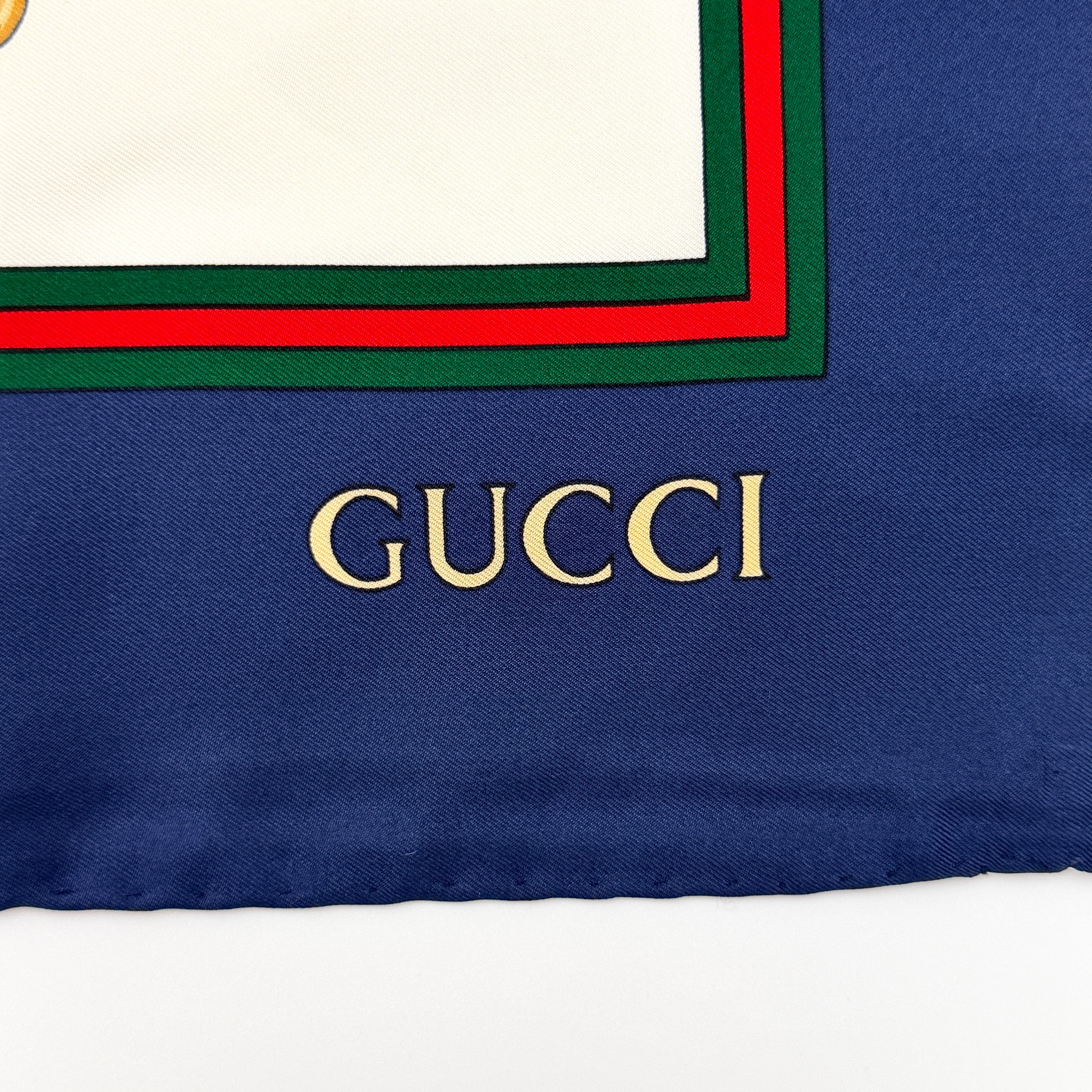 Gucci silk scarf with equestrian horsebit print, navy borders, and large GG logo displayed against a white background.