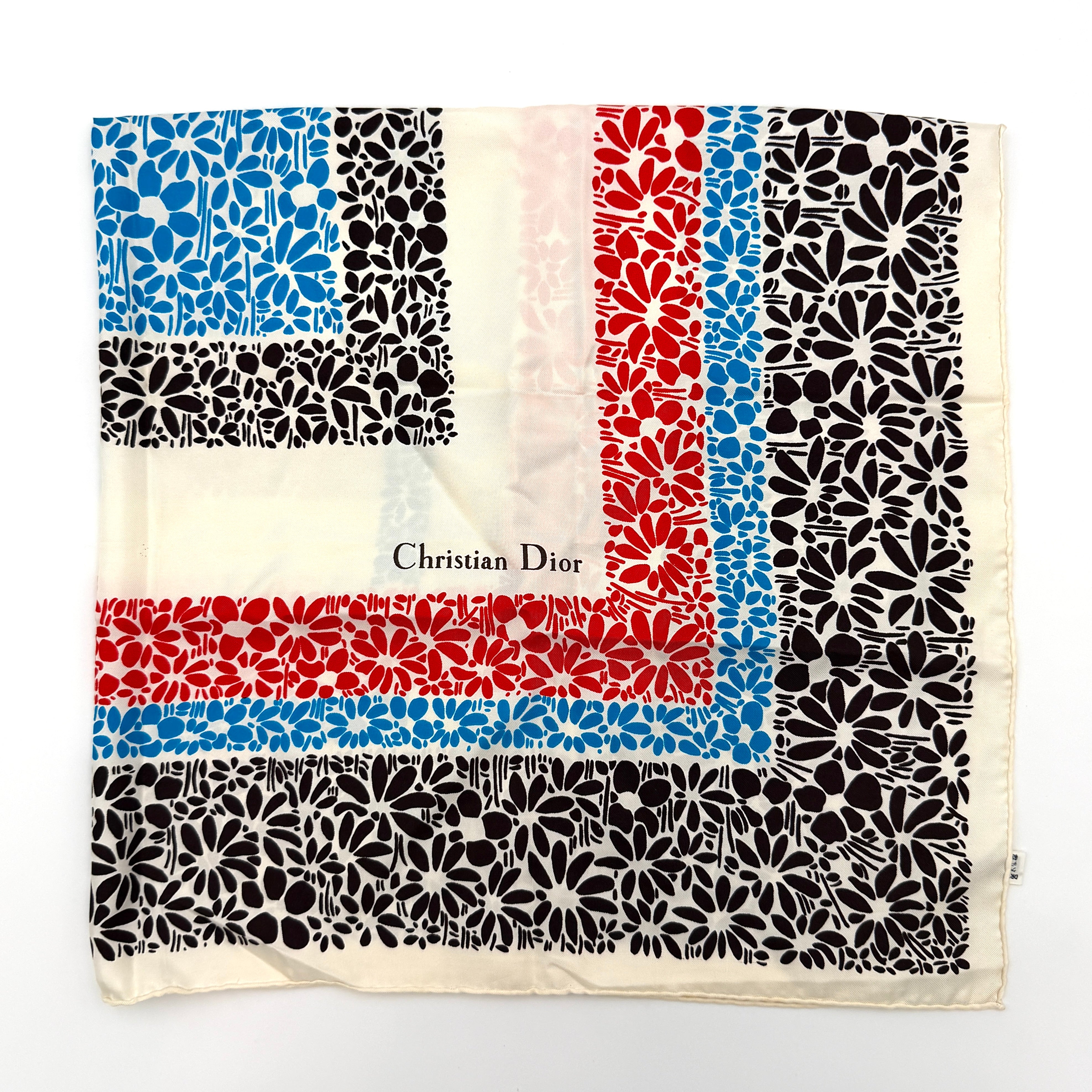 Dior silk scarf featuring a bold multicolor geometric floral pattern in red, blue, black, and ivory with the Christian Dior logo visible at the corner.