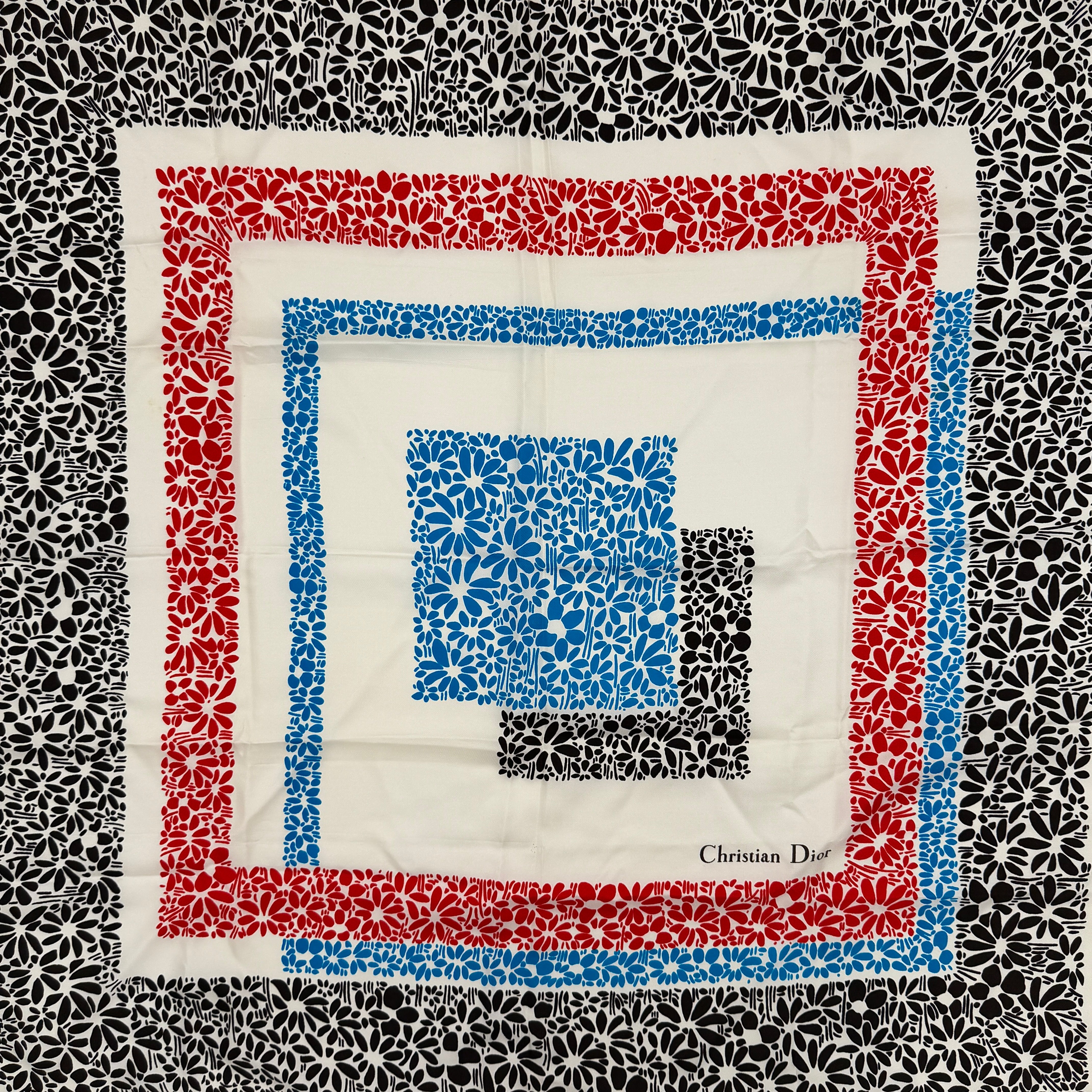 Dior silk scarf featuring a bold multicolor geometric floral pattern in red, blue, black, and ivory with the Christian Dior logo visible at the corner.