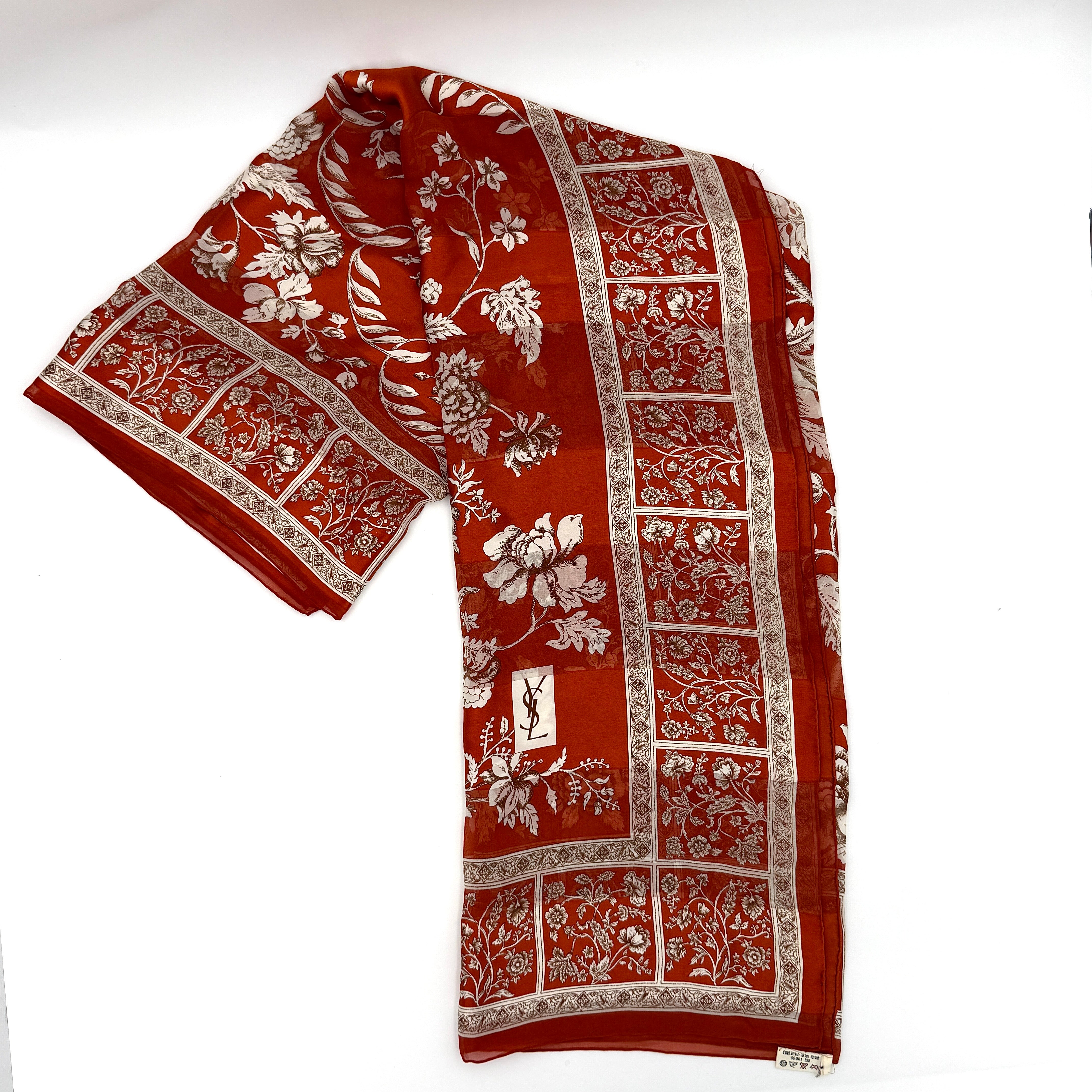 Saint Laurent silk scarf in rich red, featuring intricate cream floral designs and ornate borders with the YSL monogram visibly displayed.