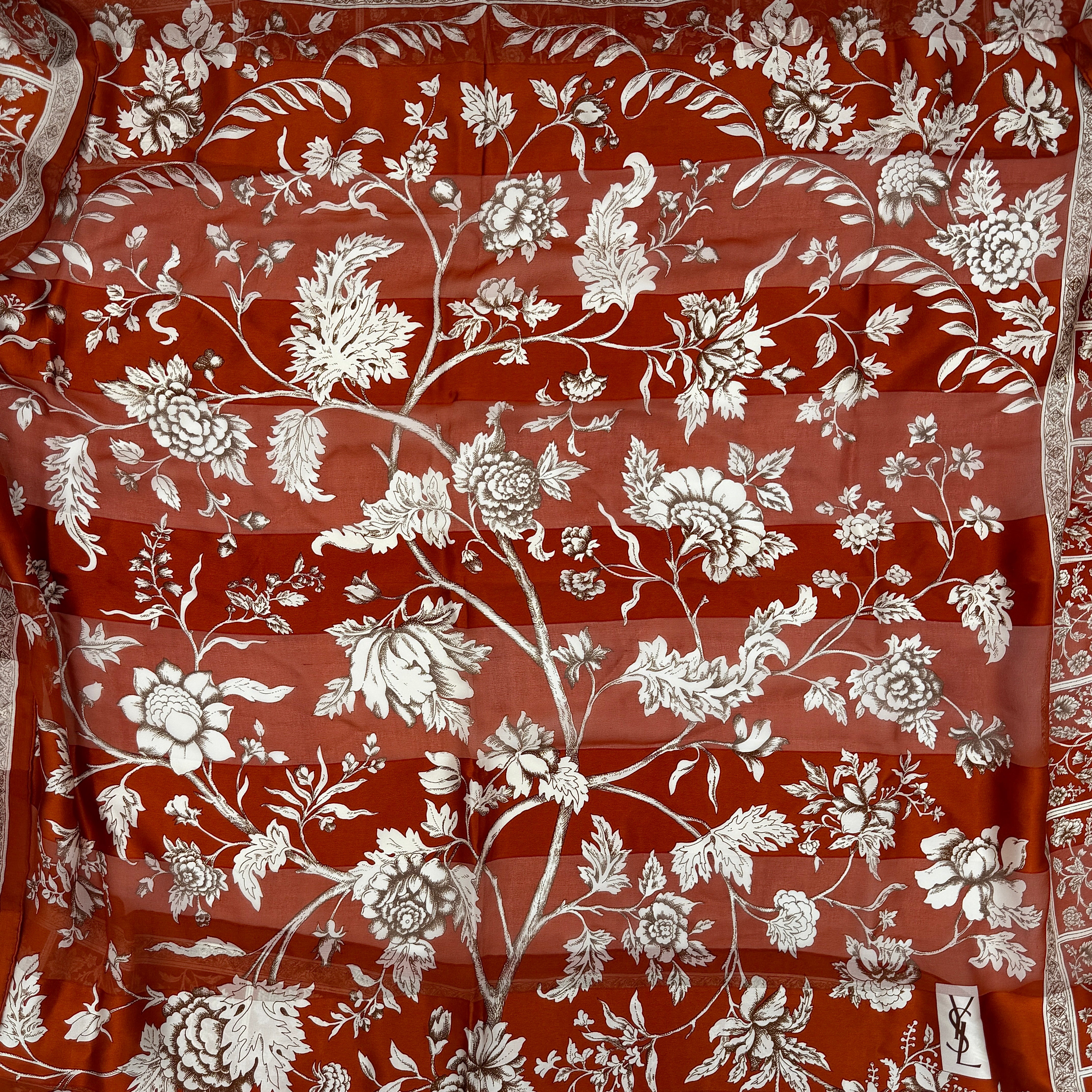 Saint Laurent silk scarf in rich red, featuring intricate cream floral designs and ornate borders with the YSL monogram visibly displayed.