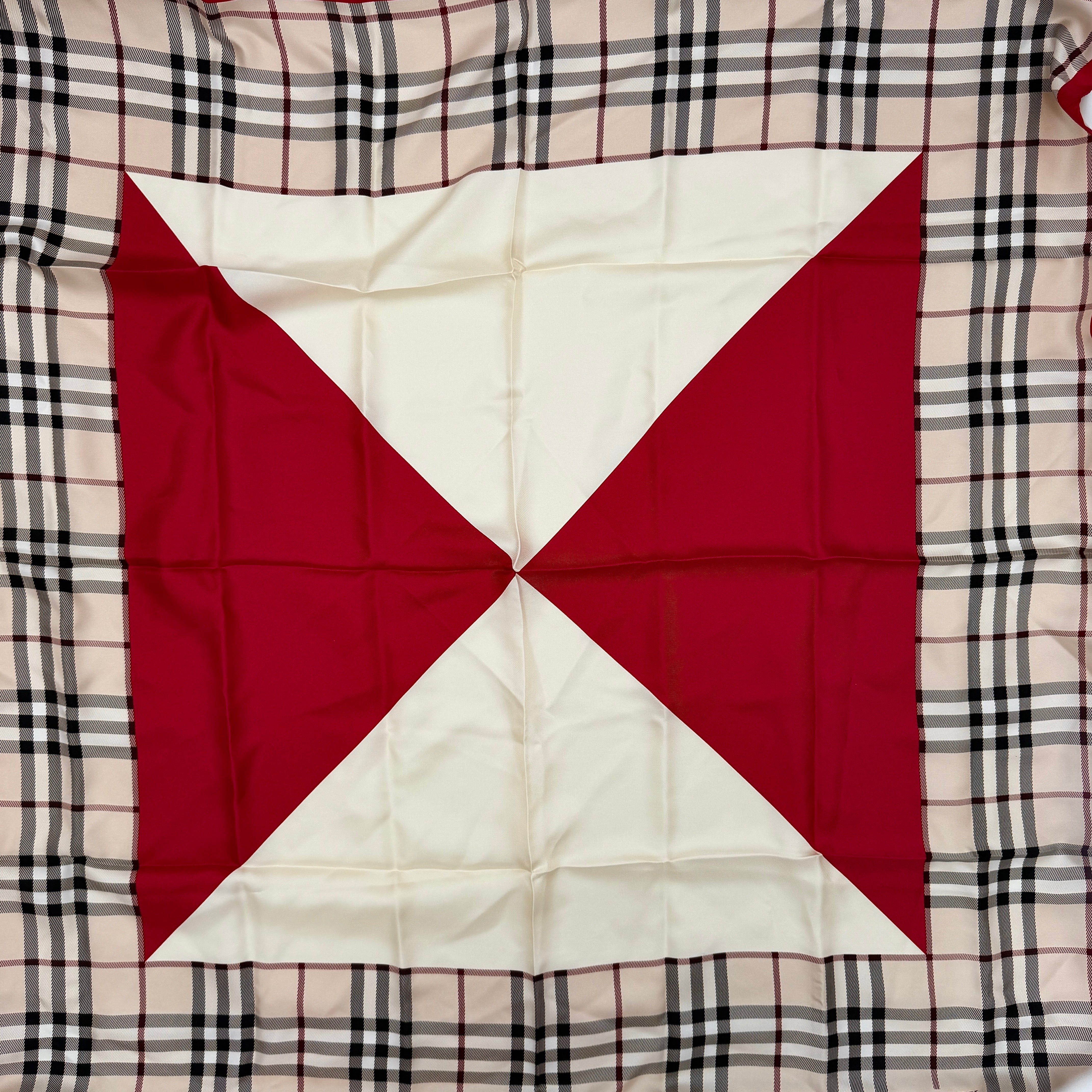 A Burberry silk scarf with beige check pattern, bold red borders, and ivory geometric panels, artfully arranged to showcase its contemporary elegance.