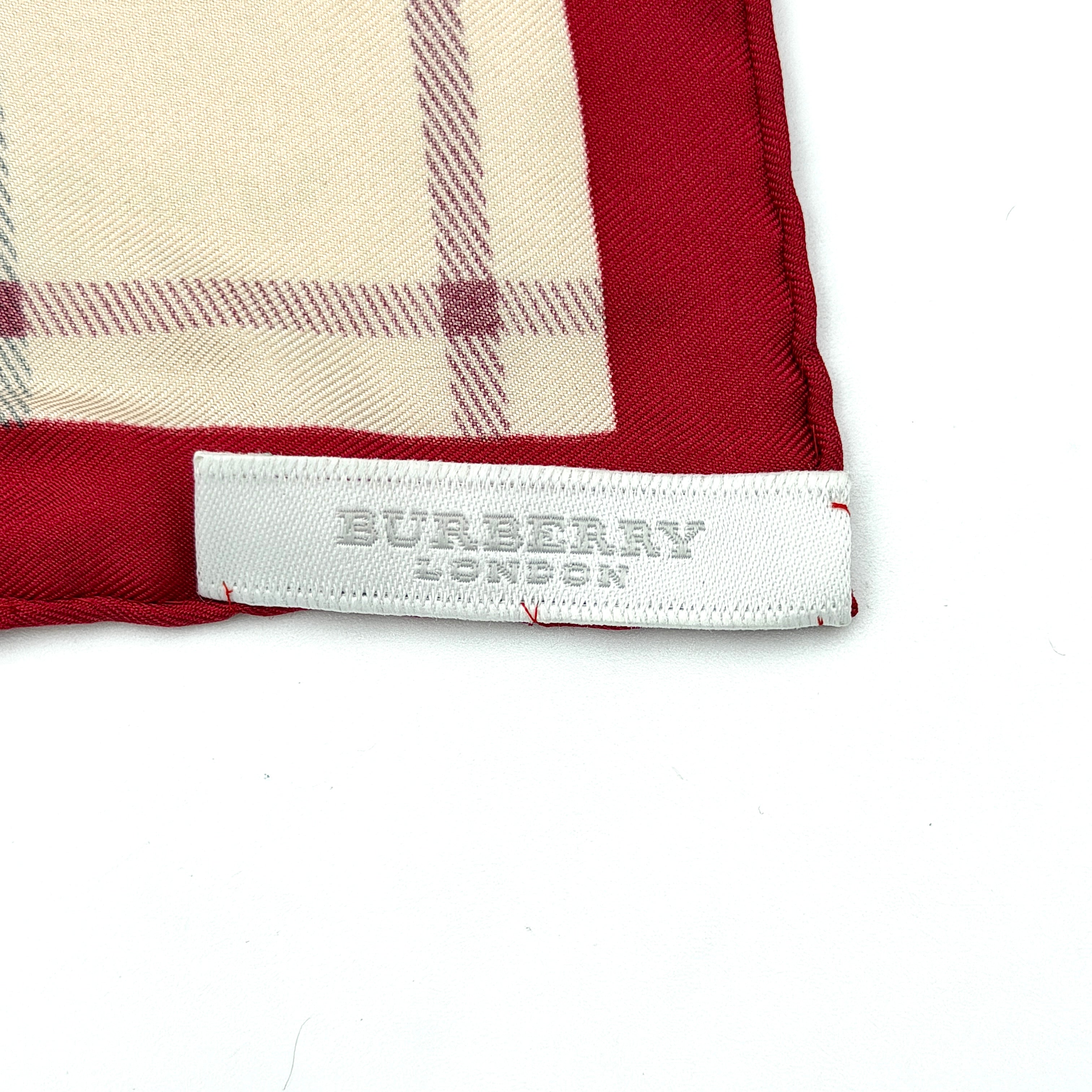 A Burberry silk scarf with beige check pattern, bold red borders, and ivory geometric panels, artfully arranged to showcase its contemporary elegance.