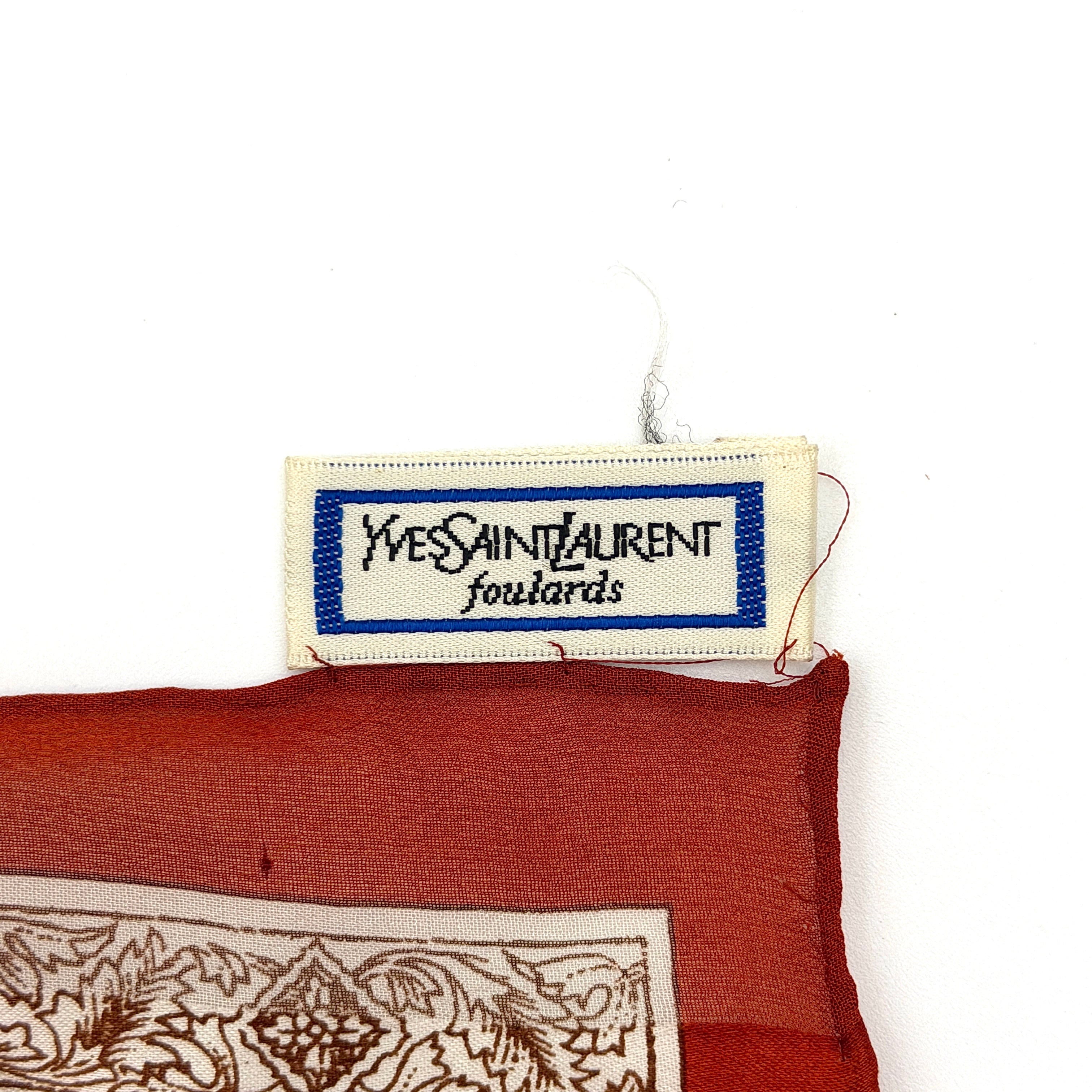 Saint Laurent silk scarf in rich red, featuring intricate cream floral designs and ornate borders with the YSL monogram visibly displayed.