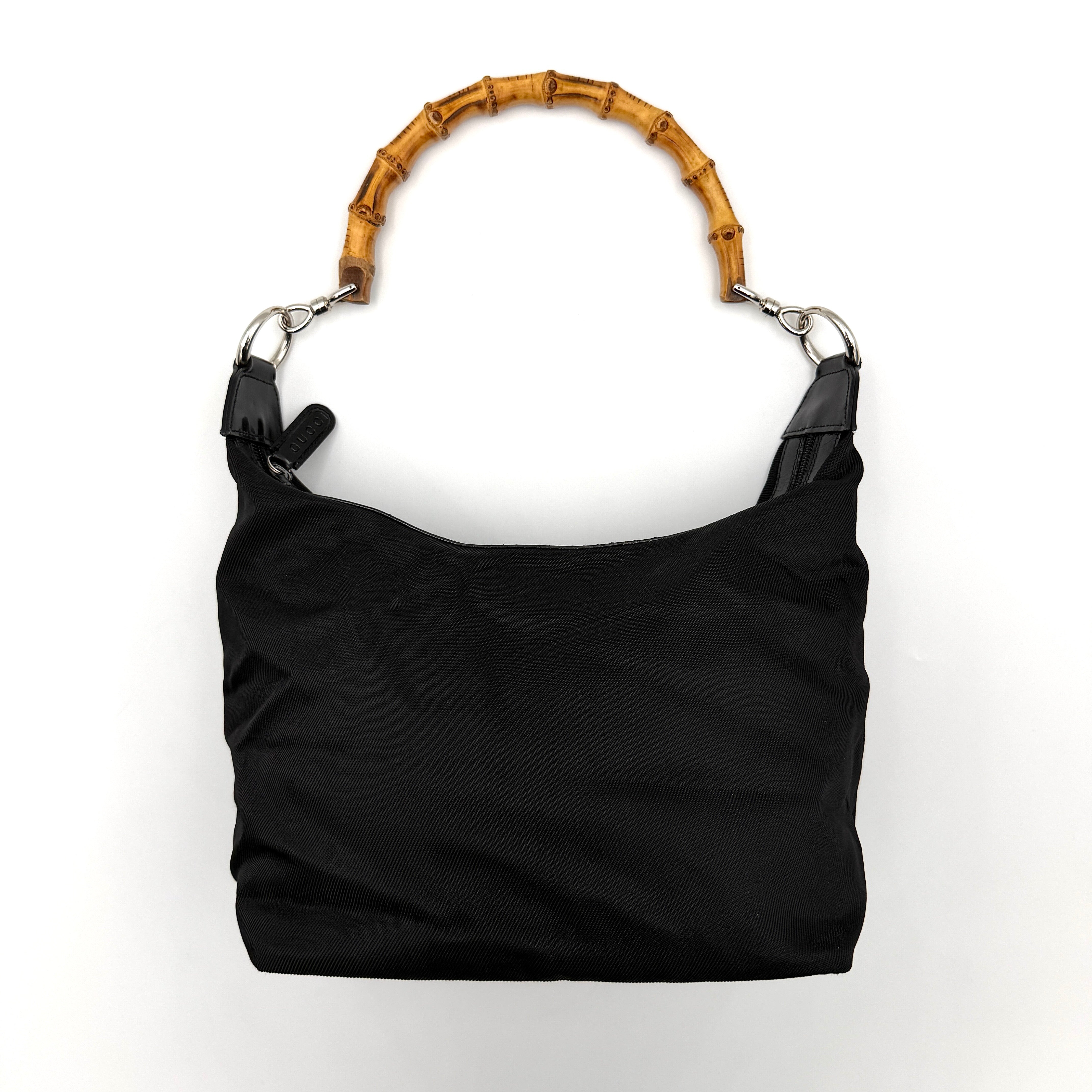 Gucci black nylon shoulder bag with a sculpted bamboo top handle and sleek silhouette against a white background.