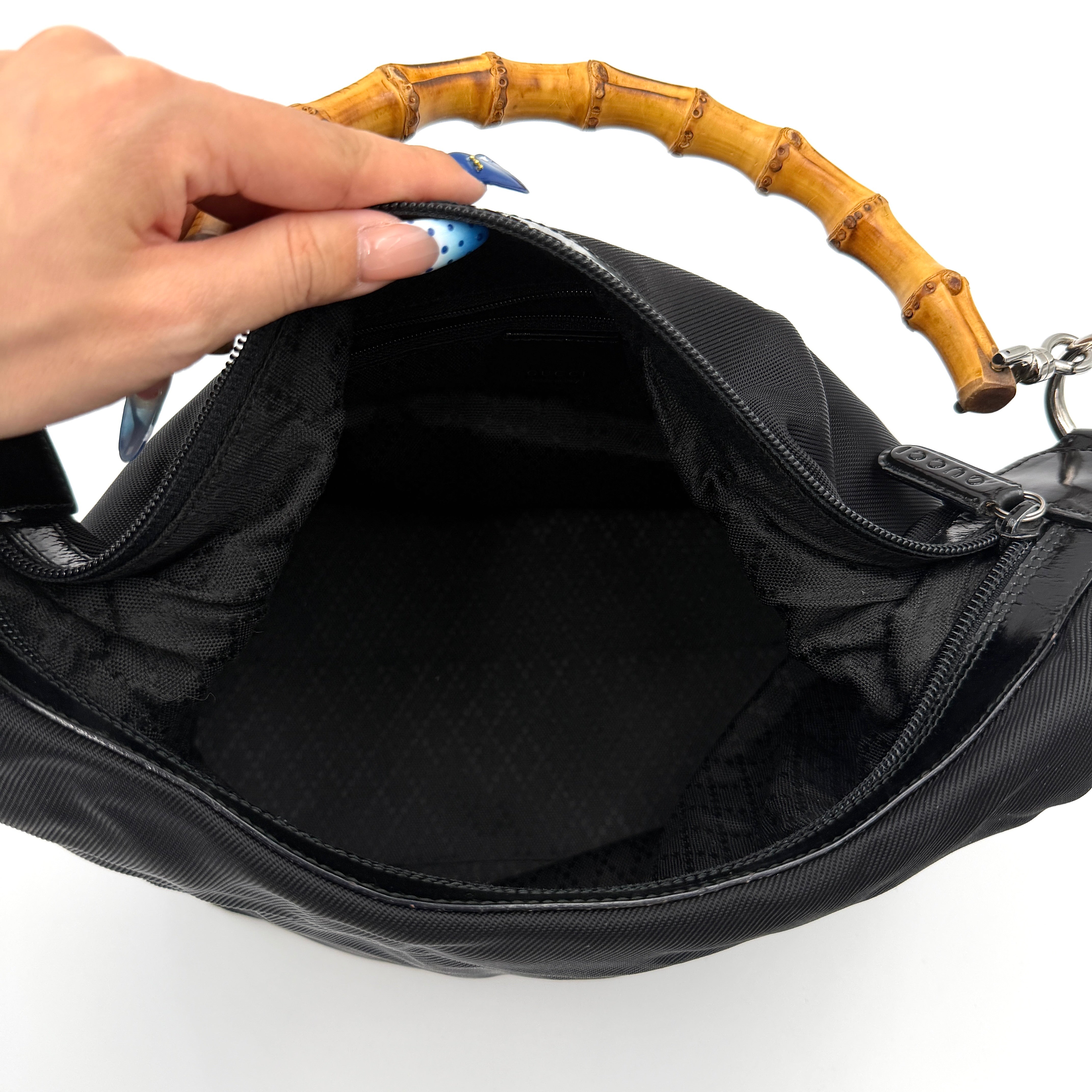 Gucci black nylon shoulder bag with a sculpted bamboo top handle and sleek silhouette against a white background.
