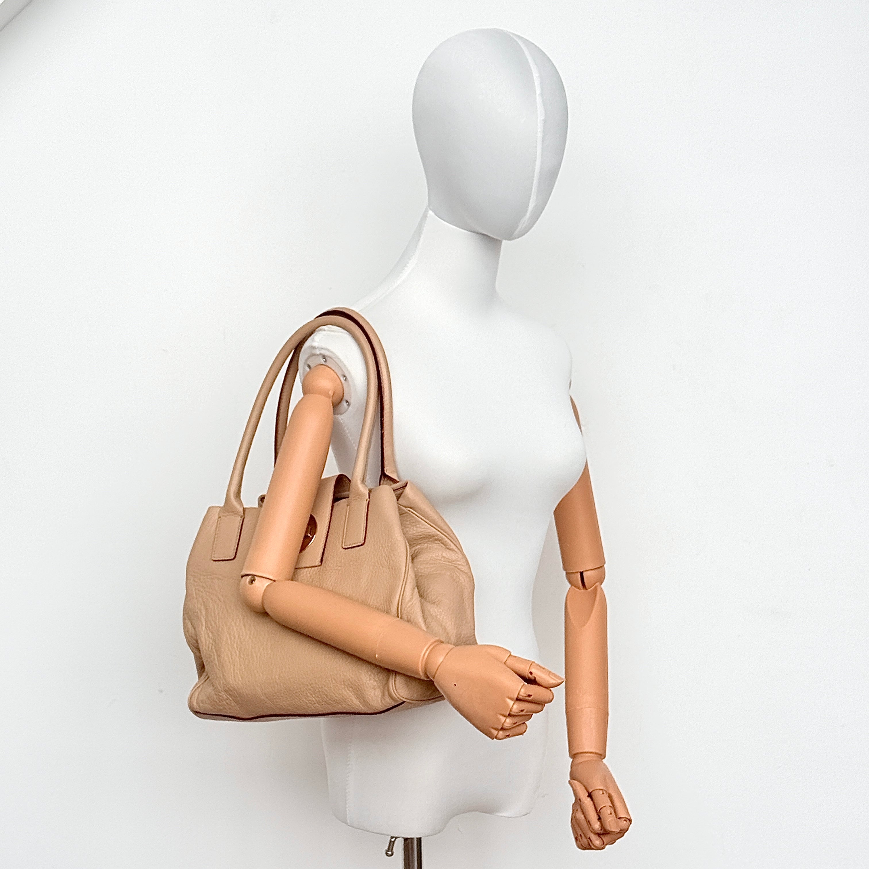 Front view of the Kate Spade Bexley Anisha beige leather satchel with turnlock closure and dual handles.