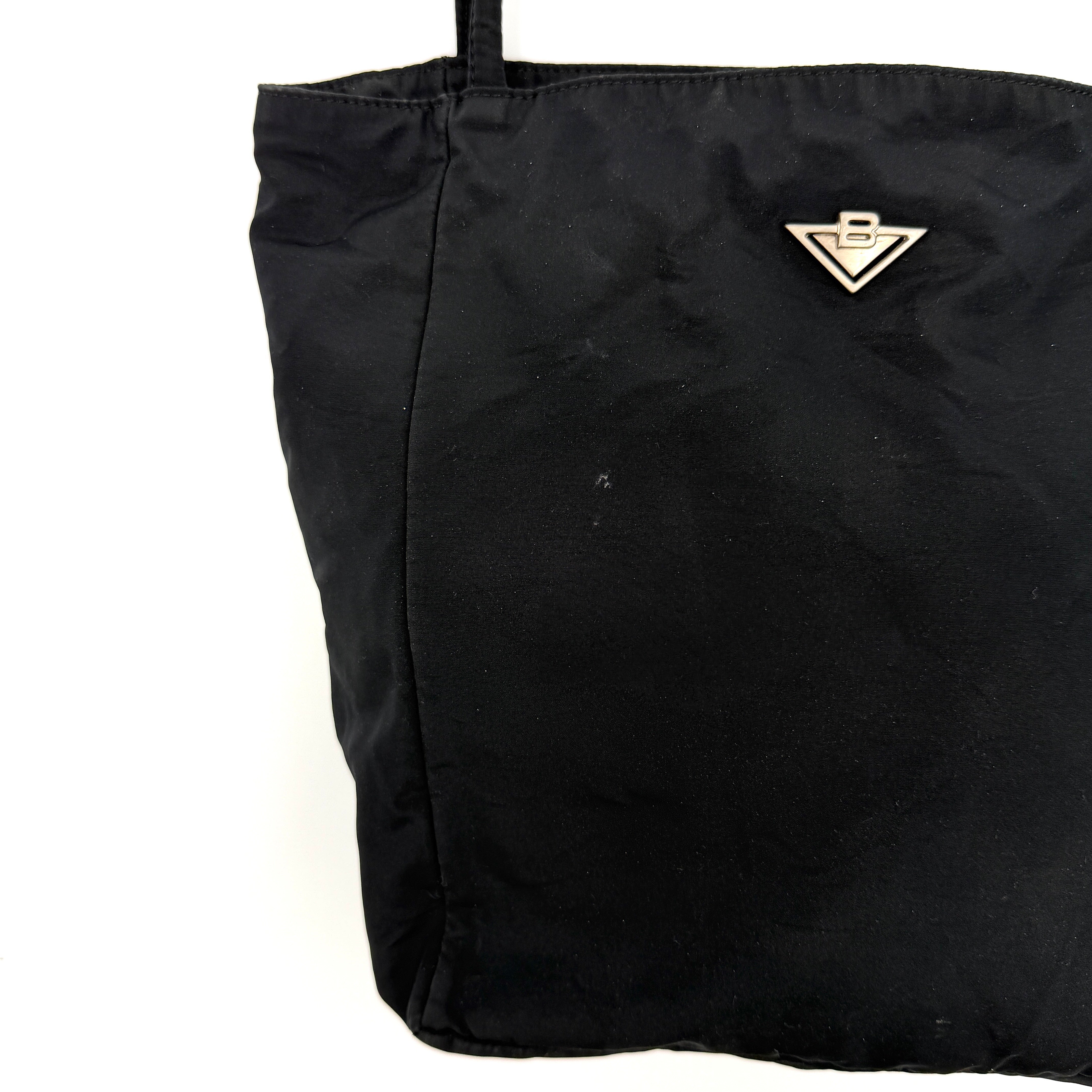 Bottega Veneta black nylon tote with structured double handles and a pale gold-tone logo plaque at the front.