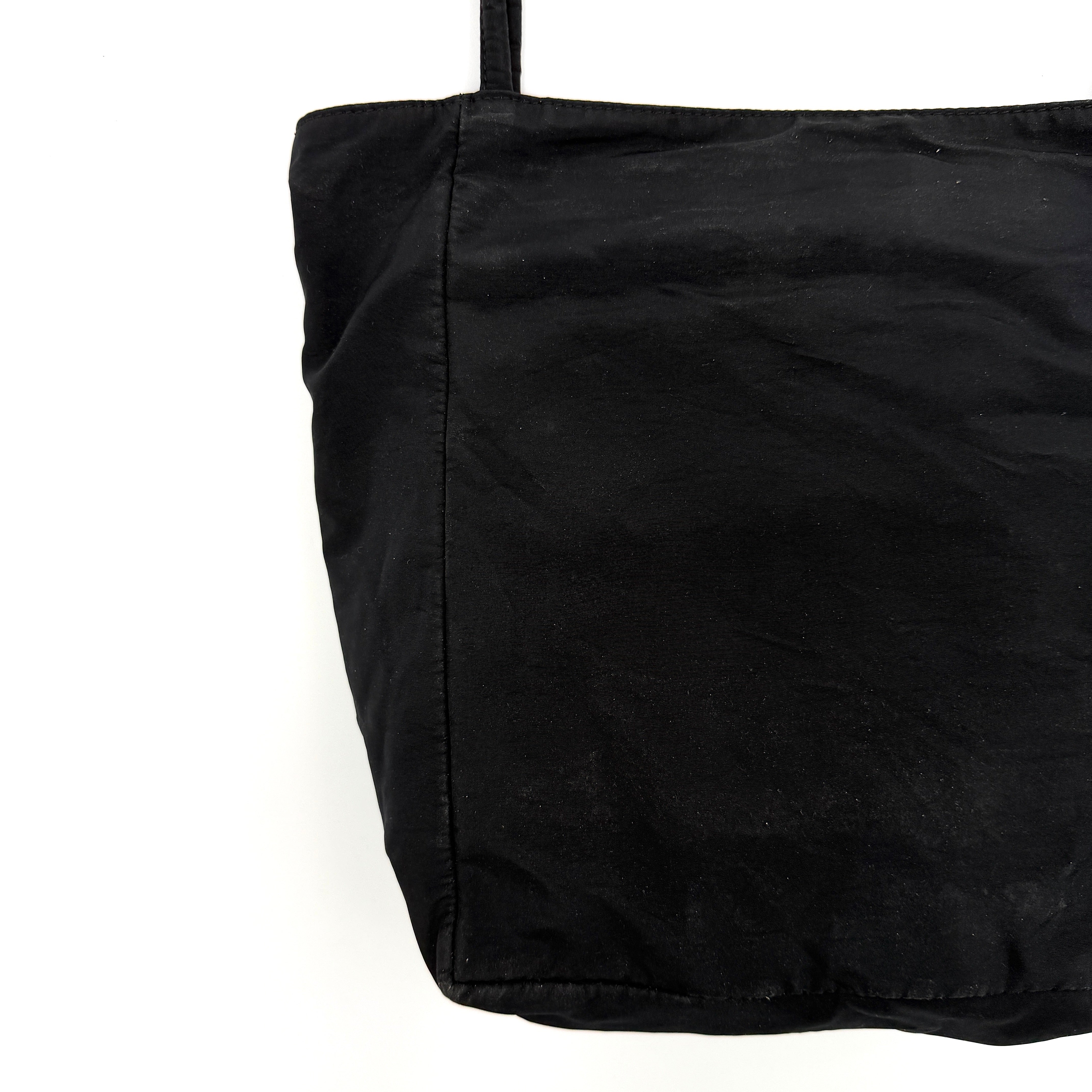 Bottega Veneta black nylon tote with structured double handles and a pale gold-tone logo plaque at the front.