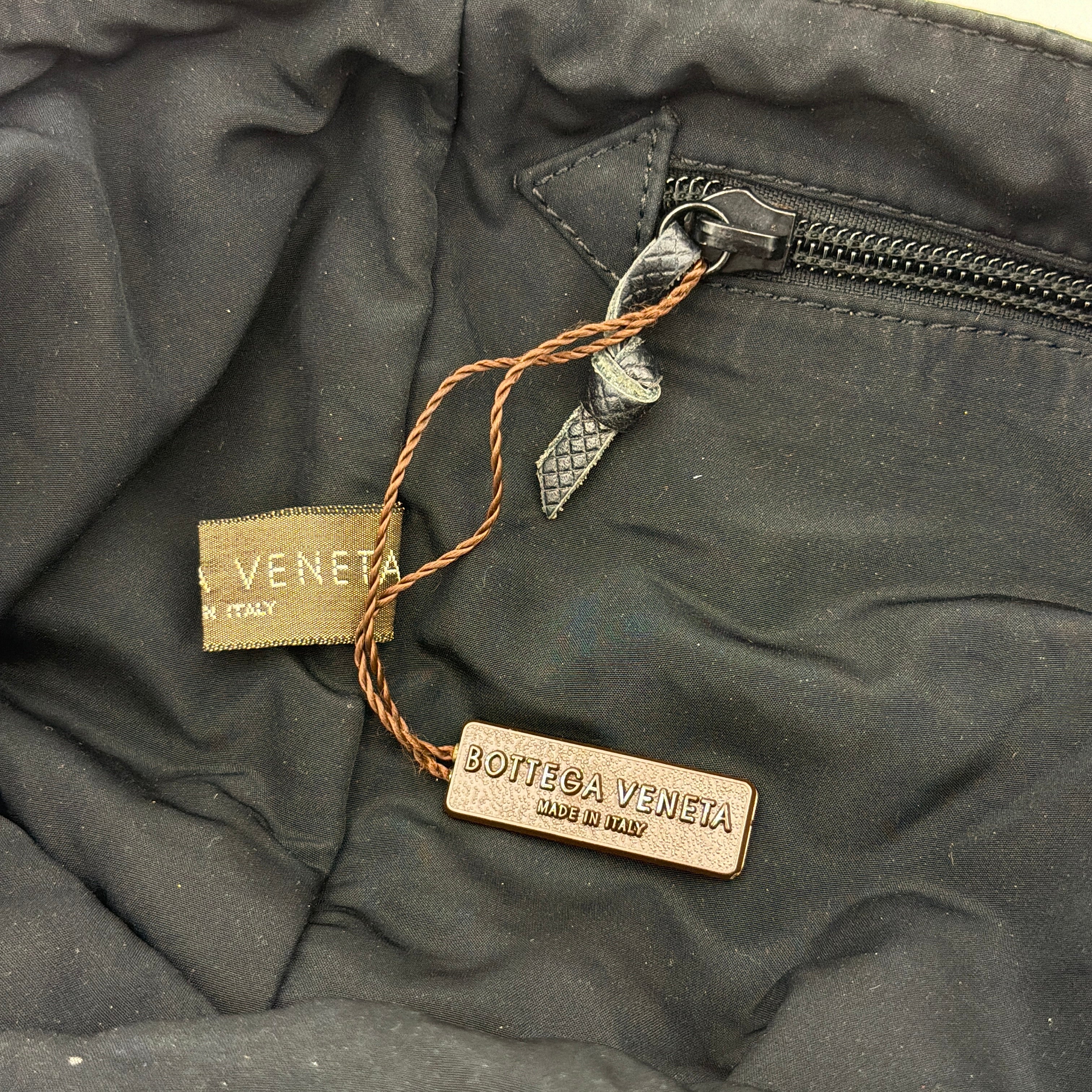Bottega Veneta black nylon tote with structured double handles and a pale gold-tone logo plaque at the front.