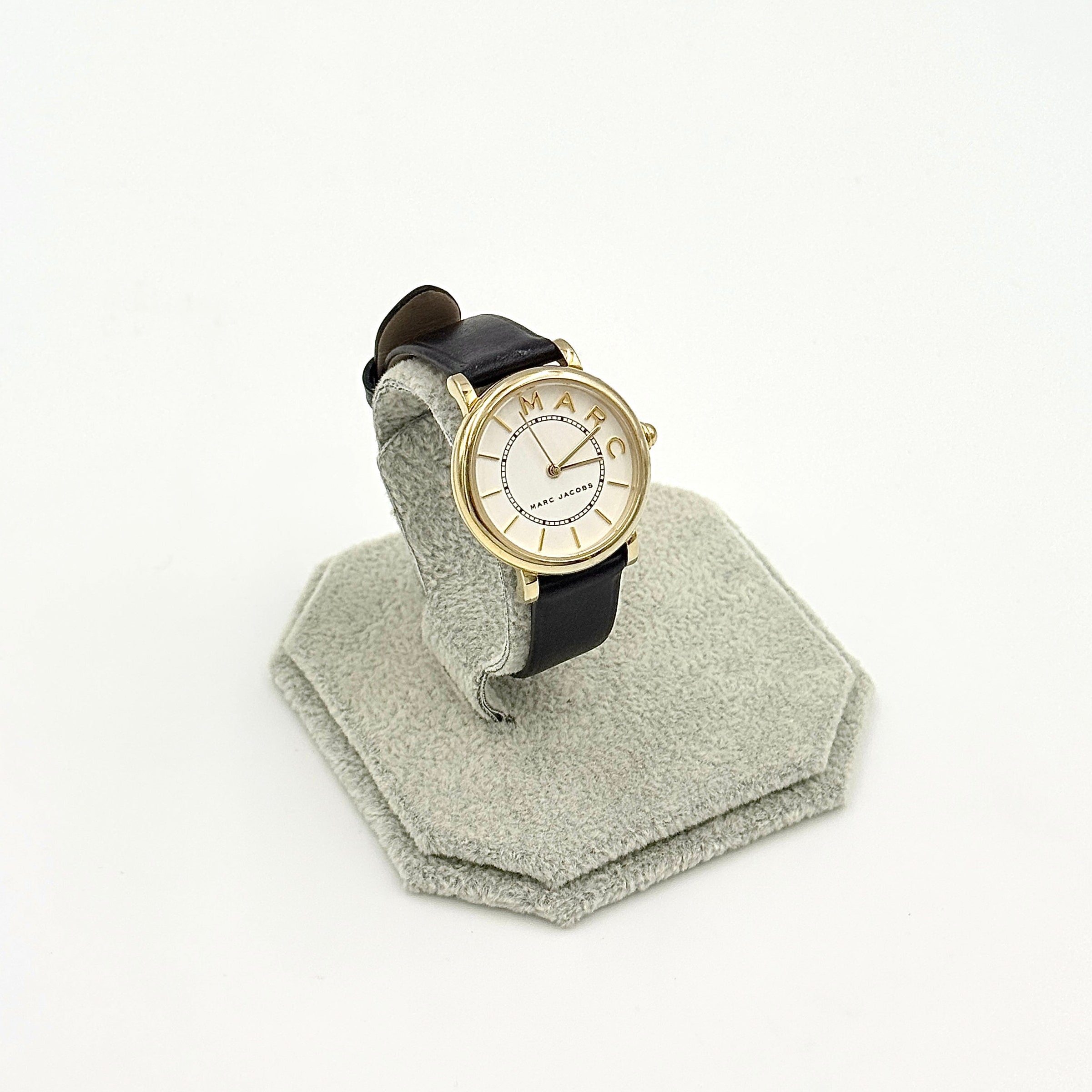 Marc Jacobs Roxy gold tone watch with black leather strap displayed on a textured stand