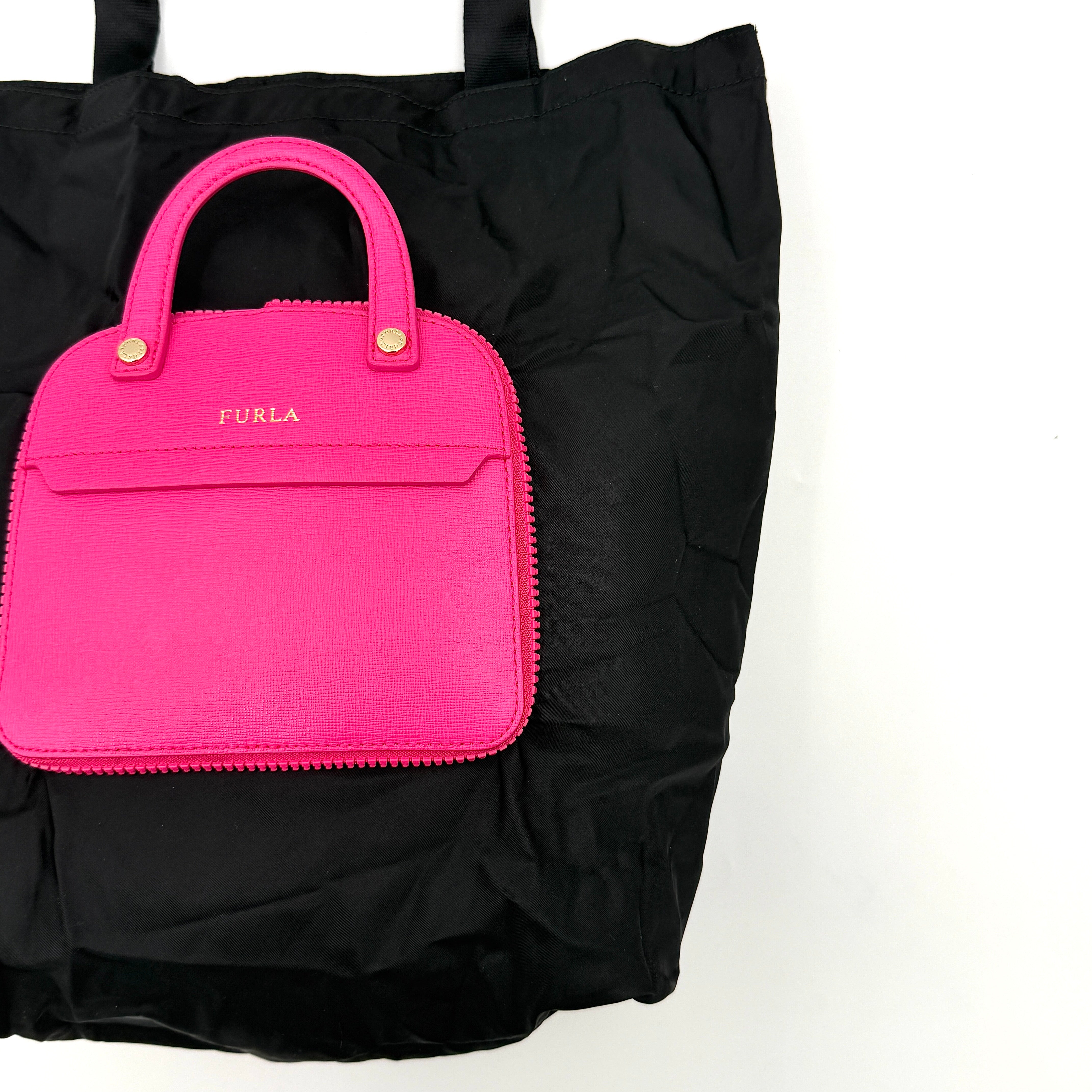 Furla black nylon tote bag with a bold pink zip pouch detail, styled as an exterior pocket, displayed flat to showcase its silhouette.