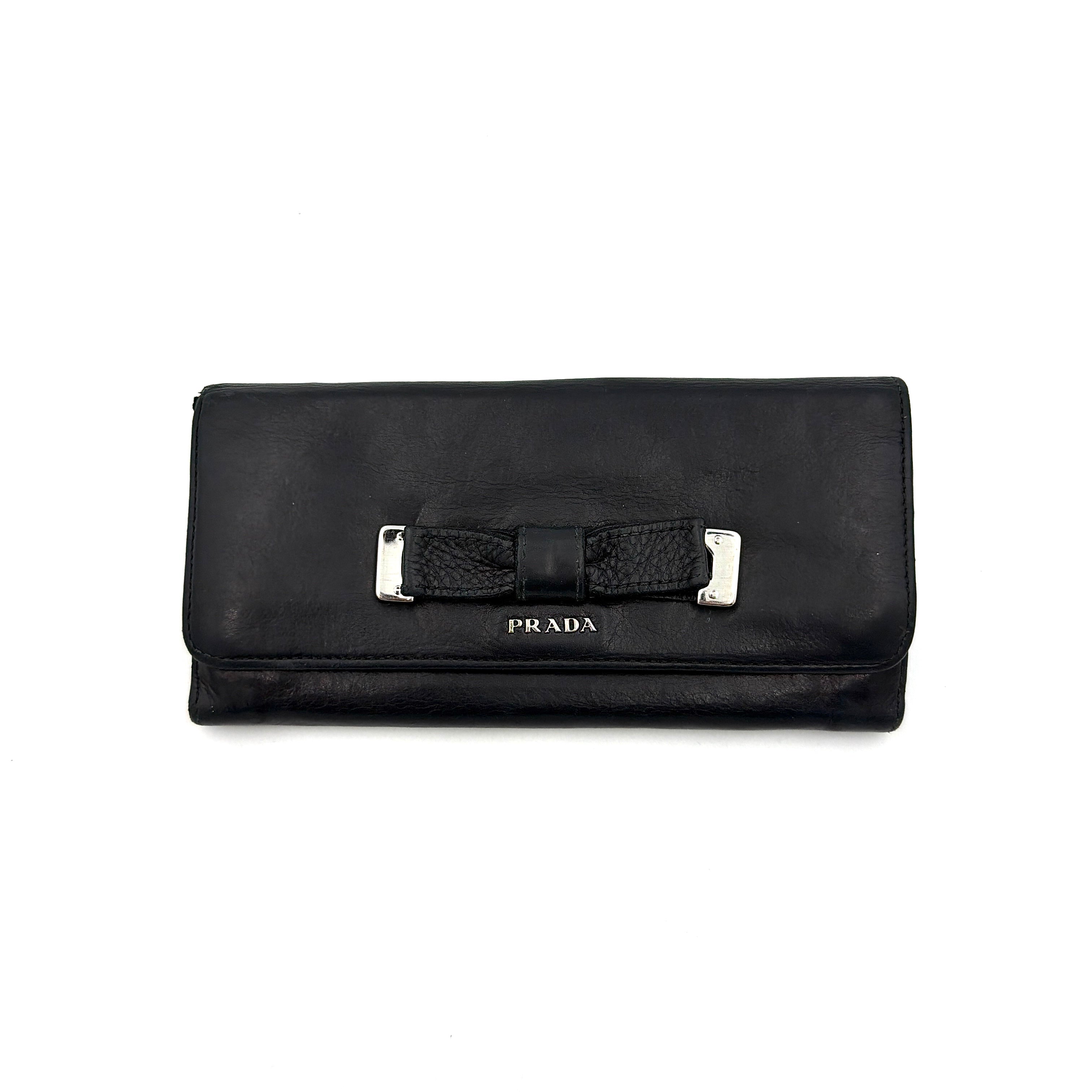 Prada Fiocco Bow Continental Wallet in black leather with a central grosgrain bow and silver-tone accents, displayed with refined simplicity.