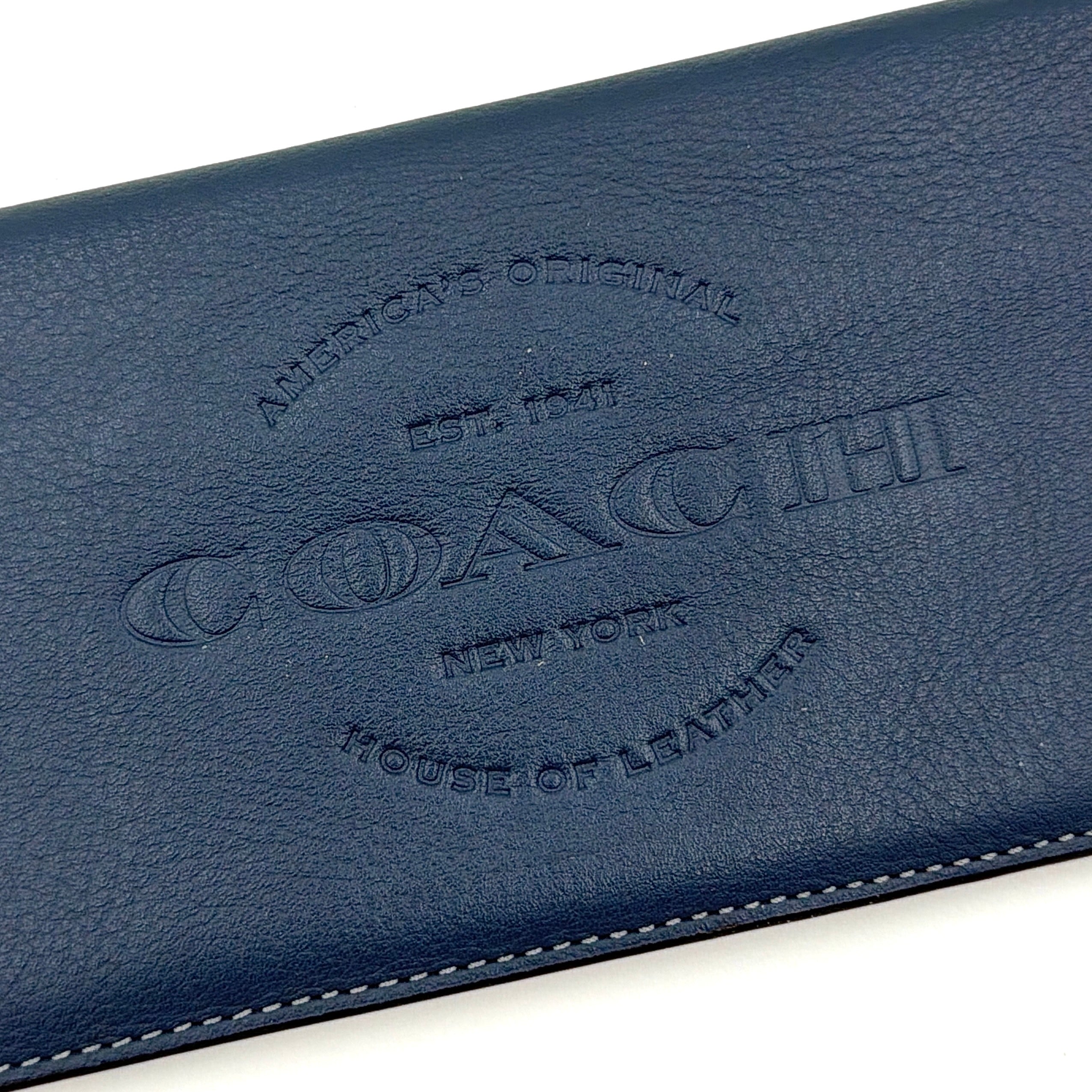 Coach Flap Long Wallet in navy blue leather with embossed logo, shown in a crisp editorial front view.