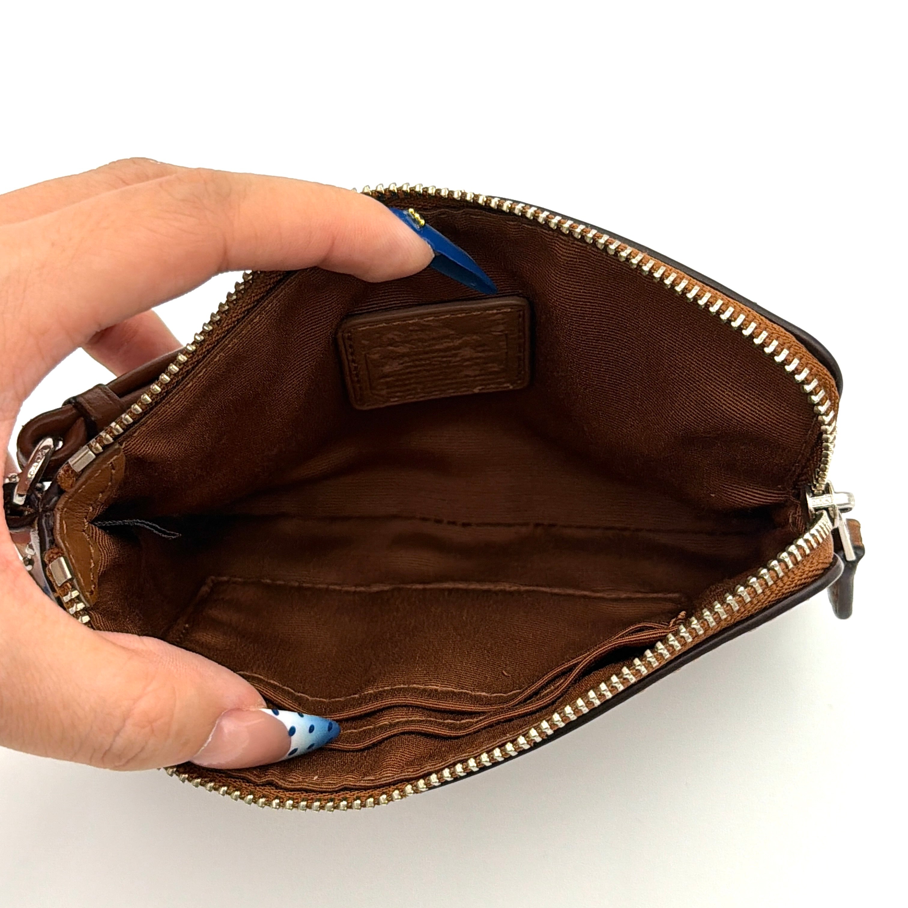 Coach Corner Zip Wristlet in smooth brown leather with silver logo and detachable wrist strap shown against a clean background.