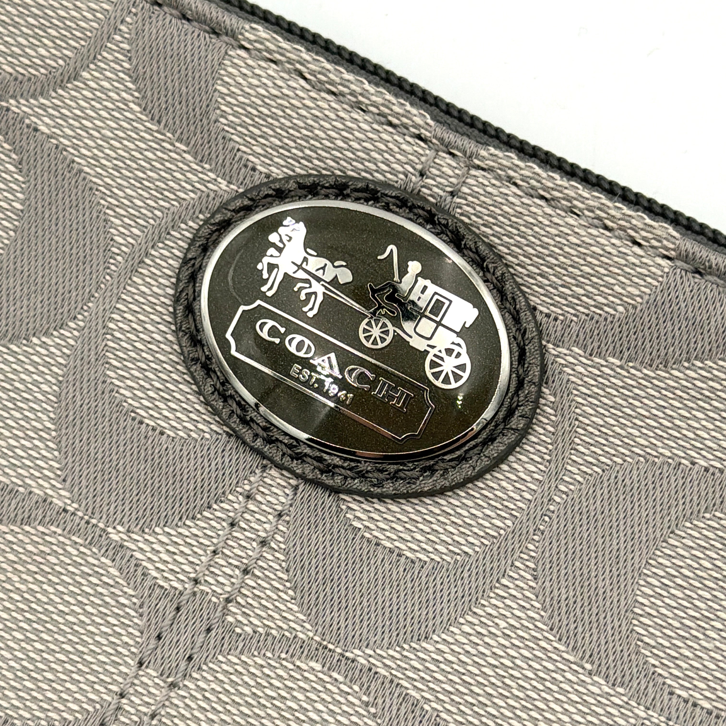 Coach Signature Canvas Corner Zip Wristlet in grey with monogram print, silver oval logo plaque, and black leather wrist strap.