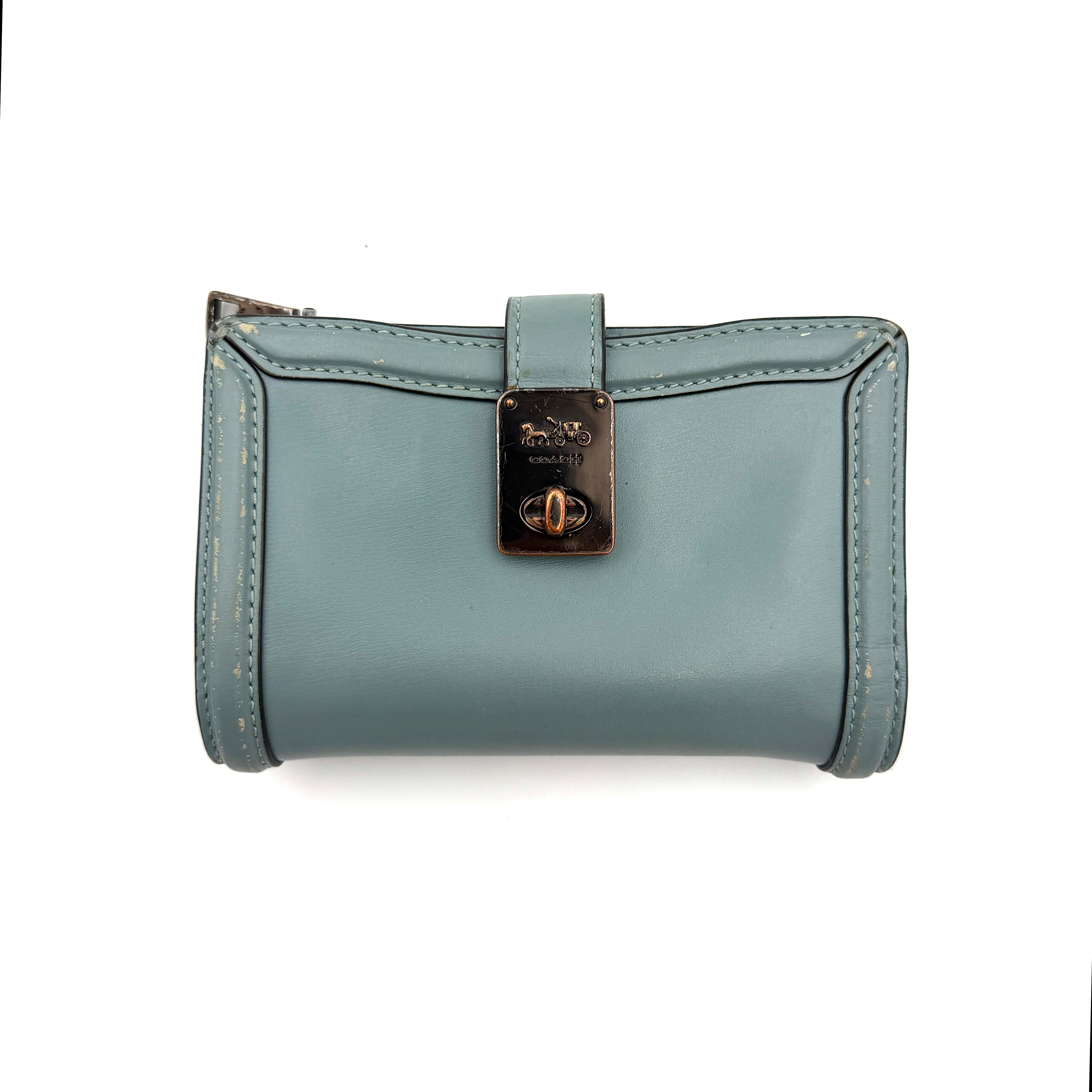 Coach Hutton Turnlock Wallet in light blue leather with signature gold turnlock clasp, showcased from the front.