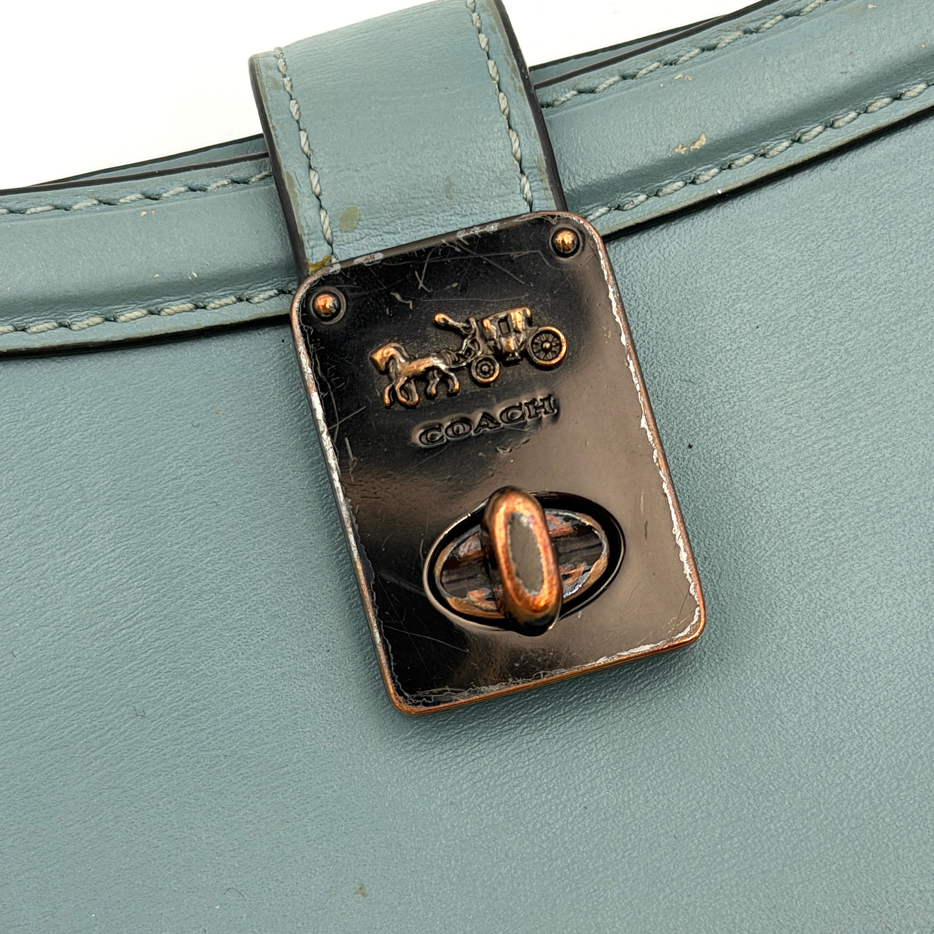 Coach Hutton Turnlock Wallet in light blue leather with signature gold turnlock clasp, showcased from the front.