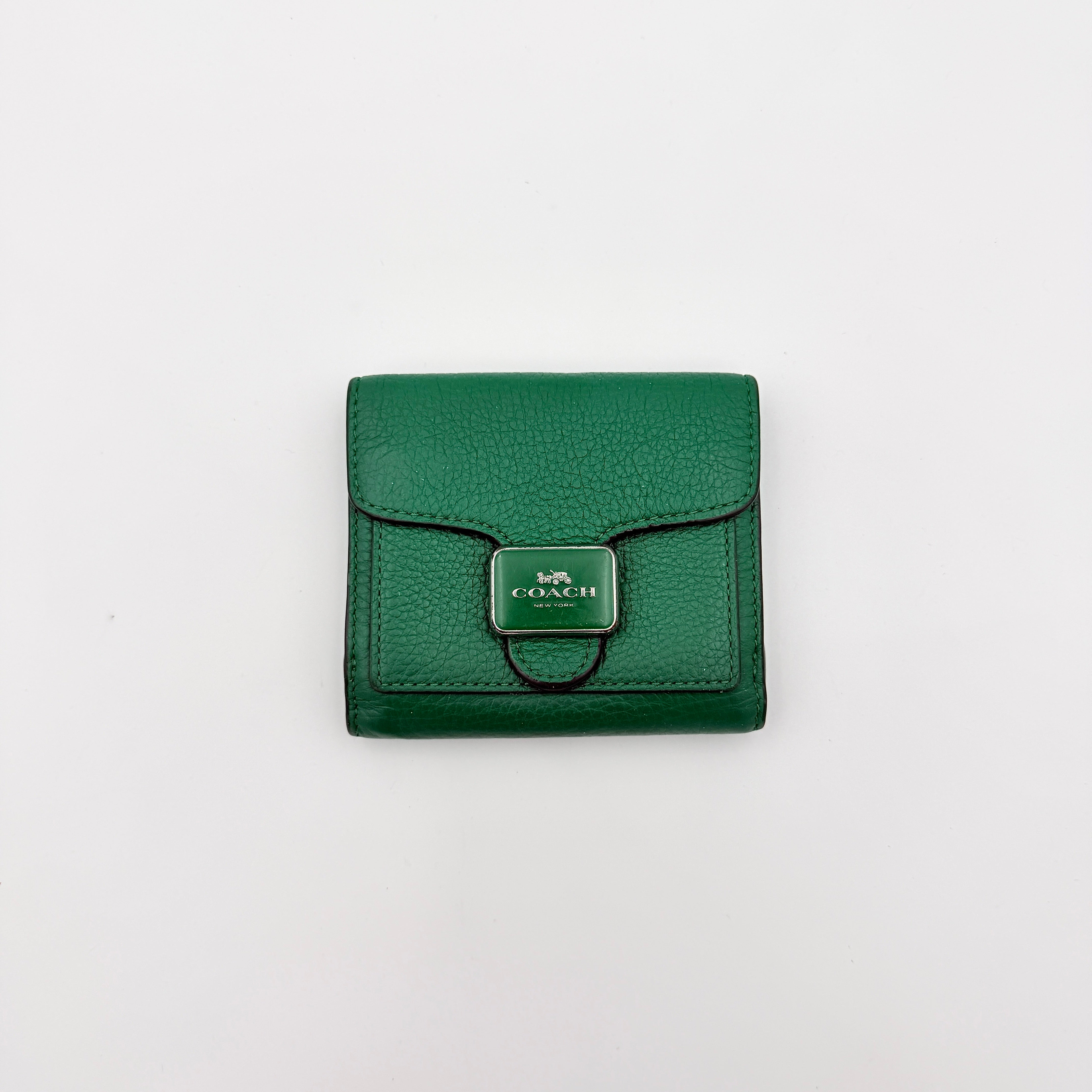 Coach Pepper Leather Wallet in emerald green pebbled leather with a front flap and enamel logo plaque, displayed neatly against a white background.