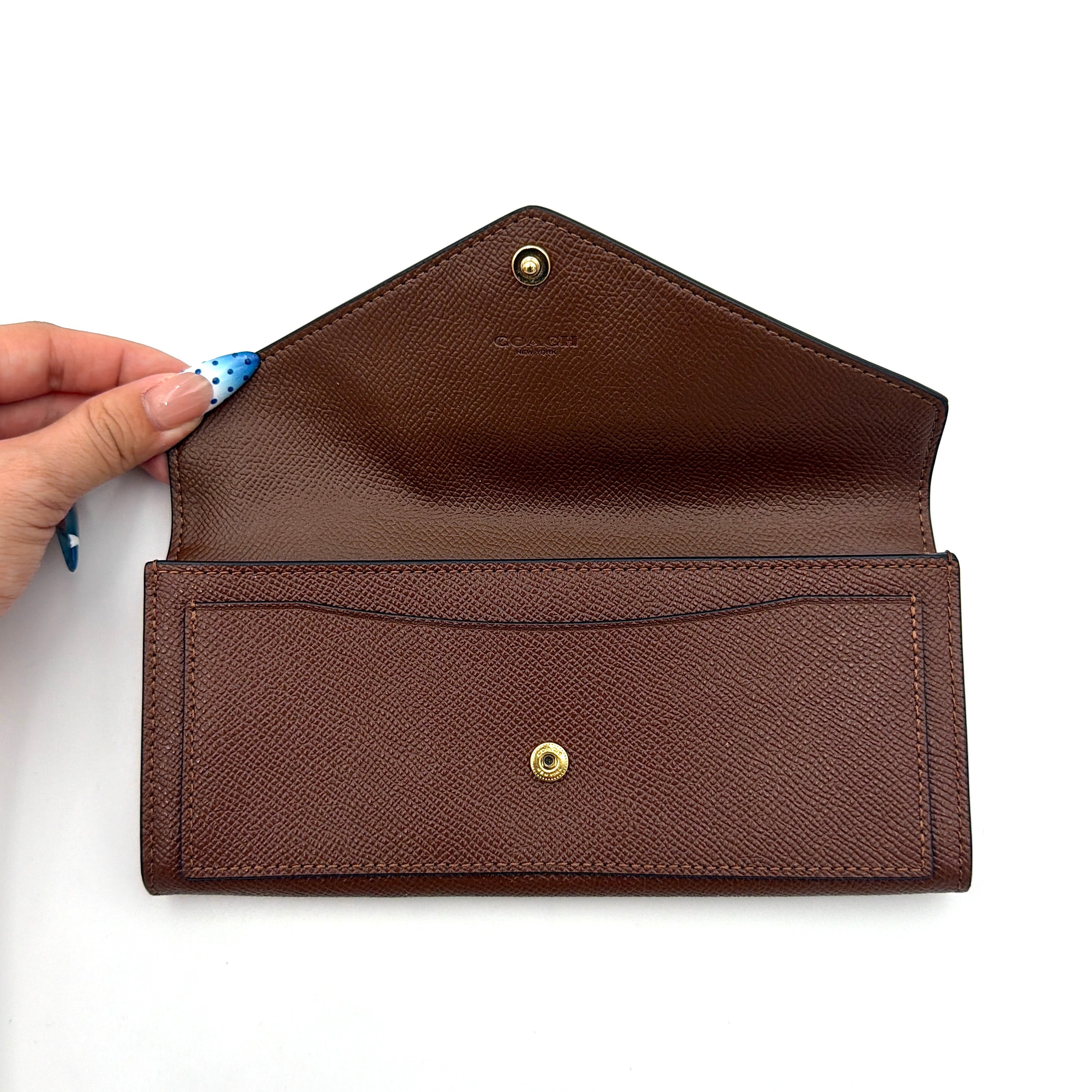 Coach brown envelope long wallet in textured leather with gold hardware, shown closed with the signature horse and carriage logo.