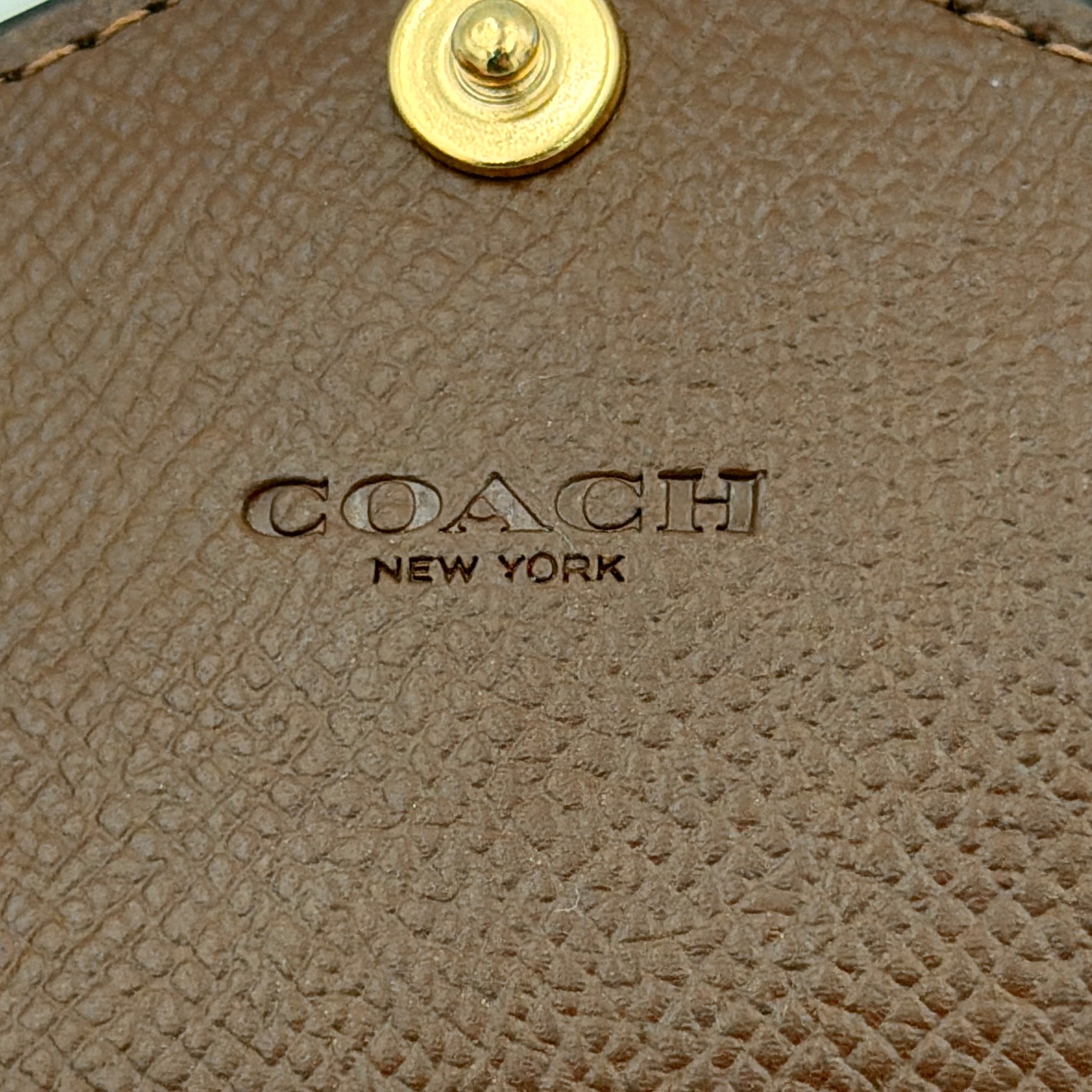 Coach brown envelope long wallet in textured leather with gold hardware, shown closed with the signature horse and carriage logo.