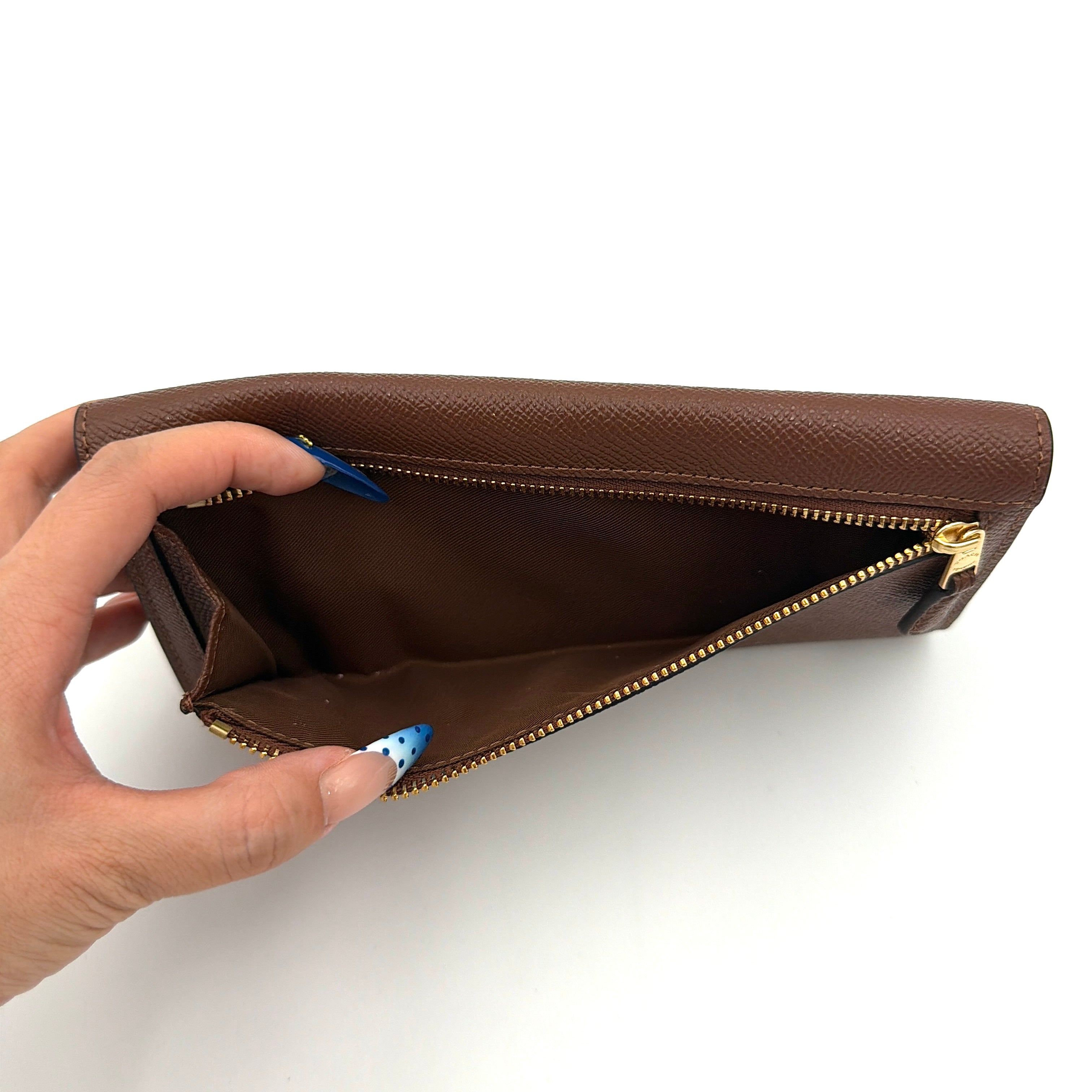 Coach brown envelope long wallet in textured leather with gold hardware, shown closed with the signature horse and carriage logo.