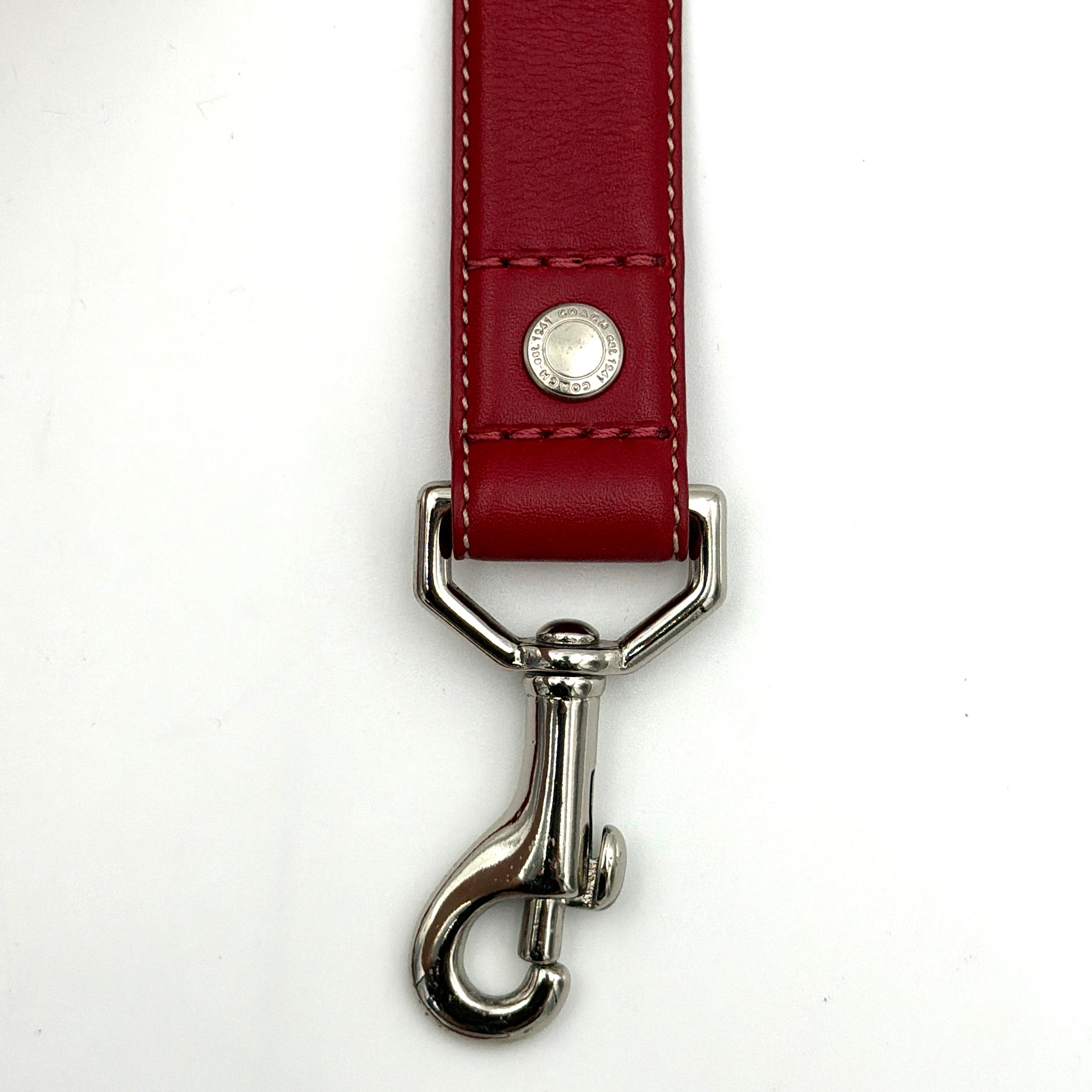 Coach leather pet leash in rich red with silvertone hardware and white contrast stitching, elegantly coiled to showcase its supple construction.
