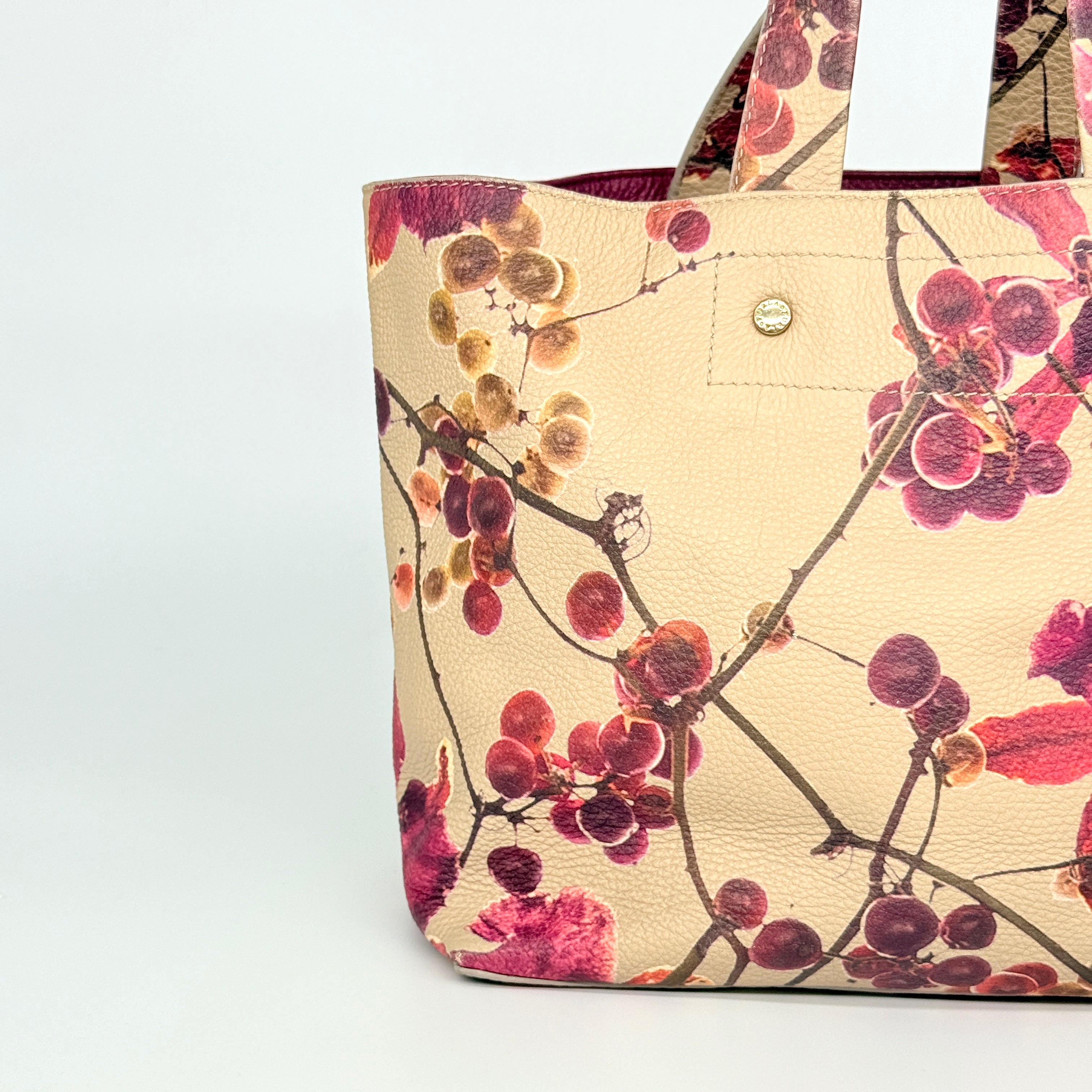 Furla beige leather tote bag adorned with a bold magenta and plum floral print, featuring structured short handles.