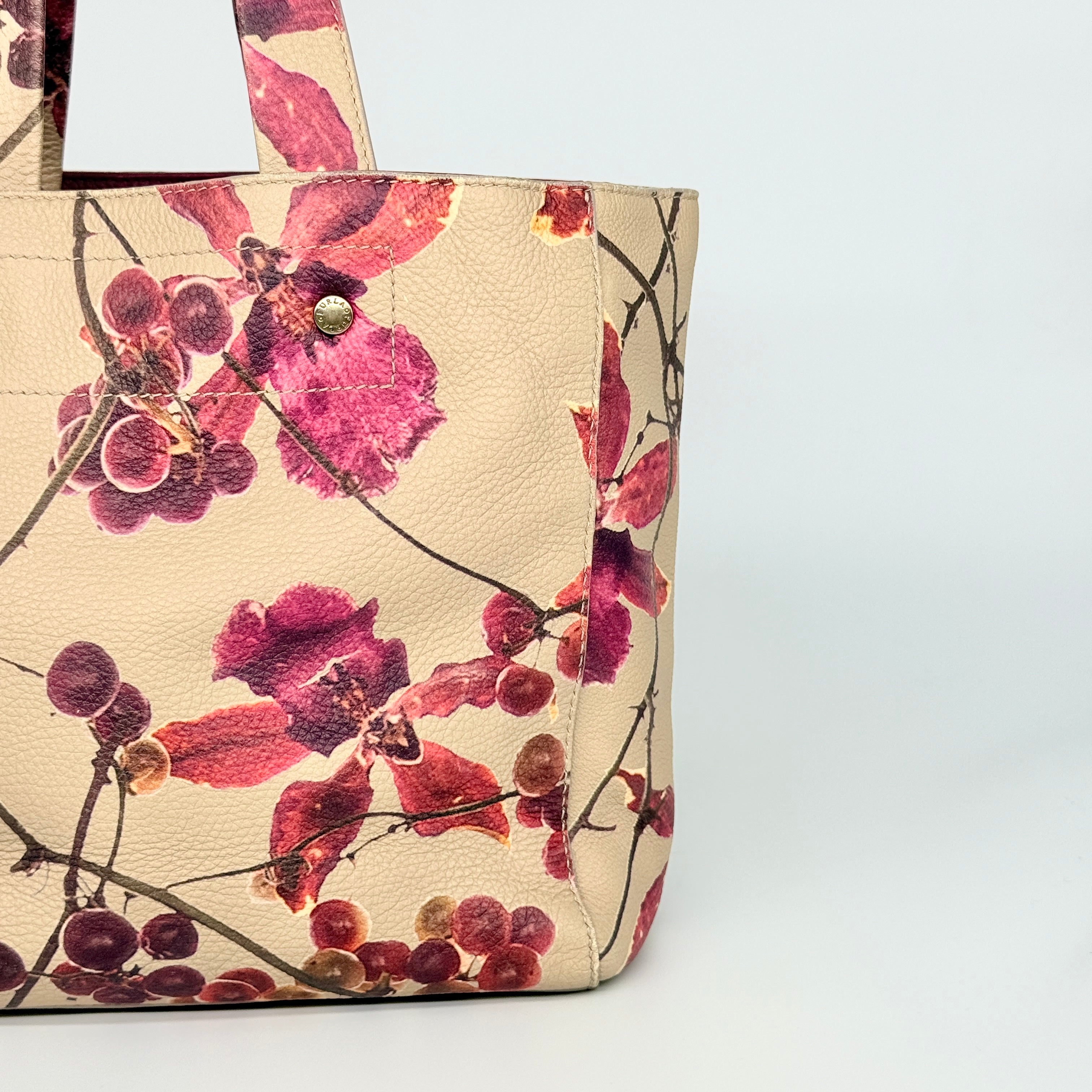Furla beige leather tote bag adorned with a bold magenta and plum floral print, featuring structured short handles.