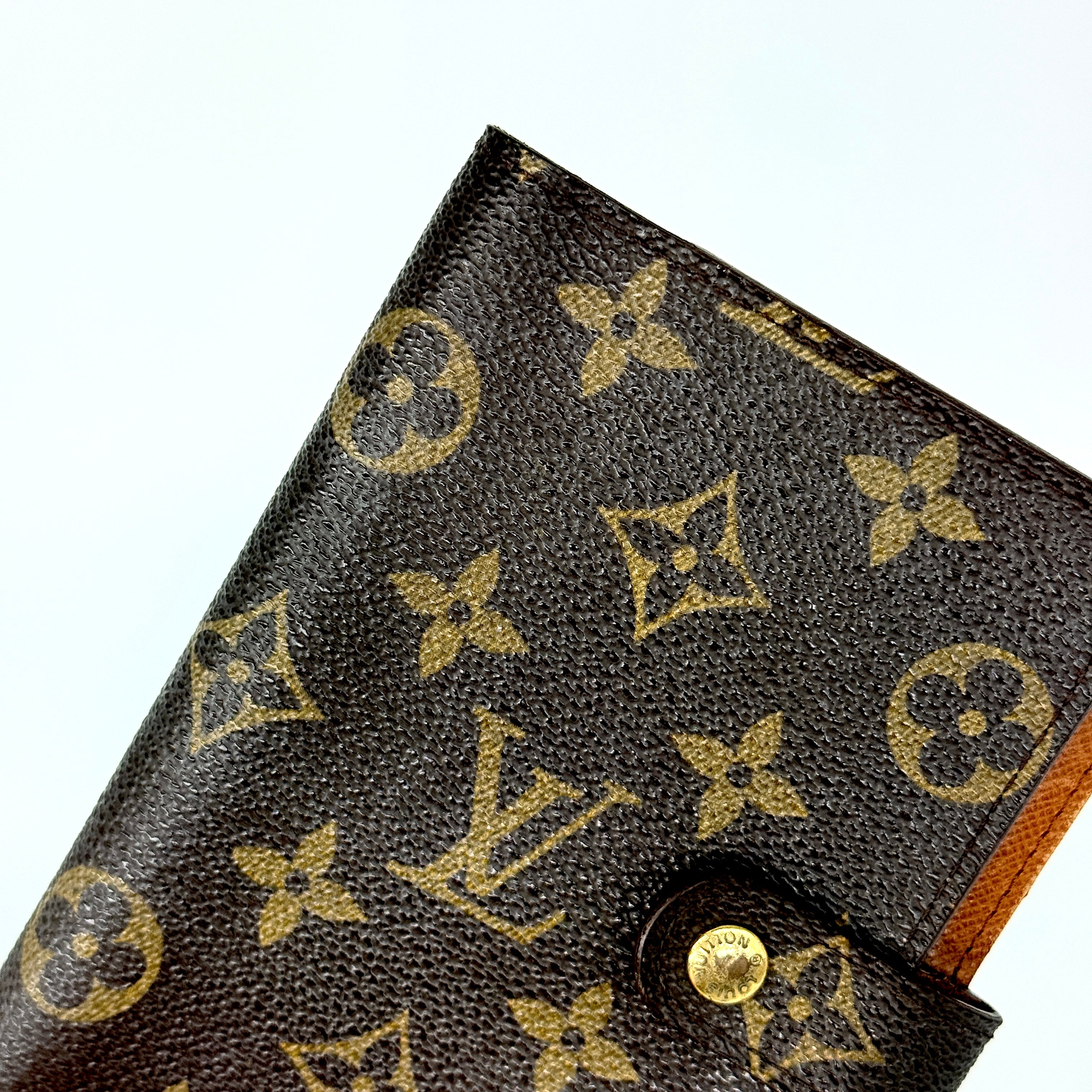 Louis Vuitton Monogram Agenda Cover in brown canvas with gold snap closure, displayed against a white background.